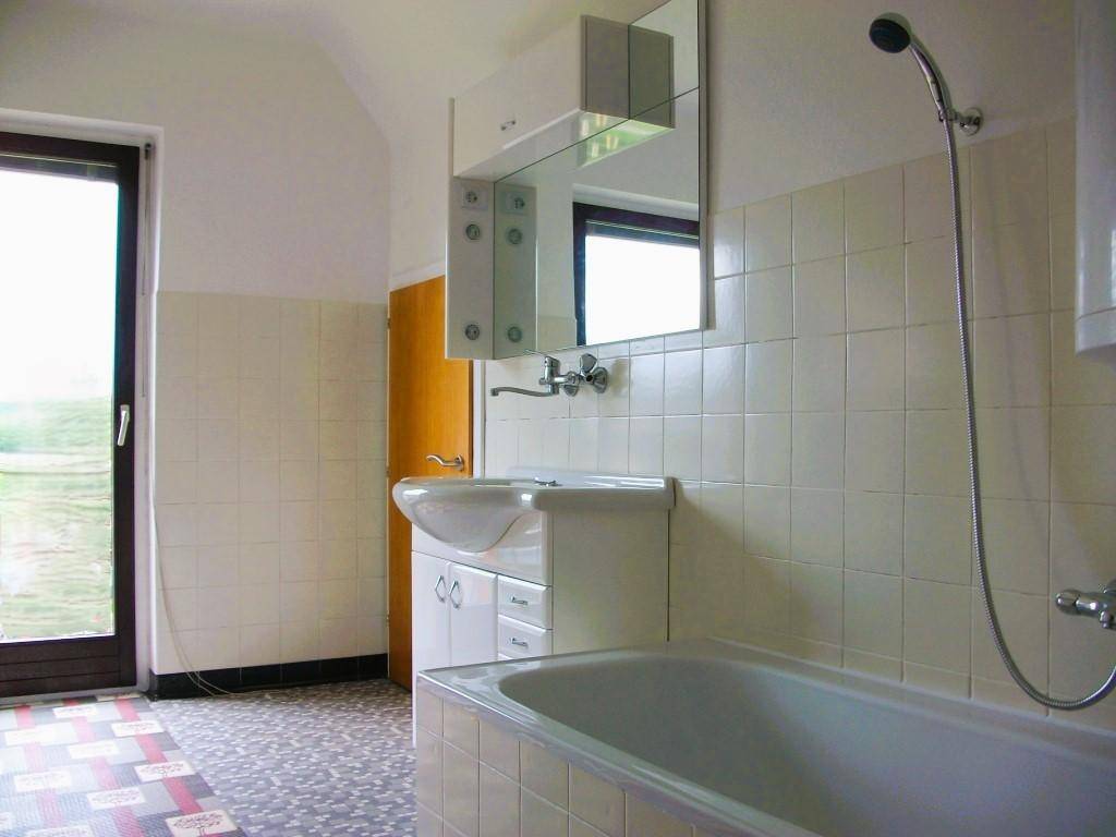 Badezimmer mit Badewanne, Waschbecken und Spiegelschrank, sowie einer Tür nach draußen.