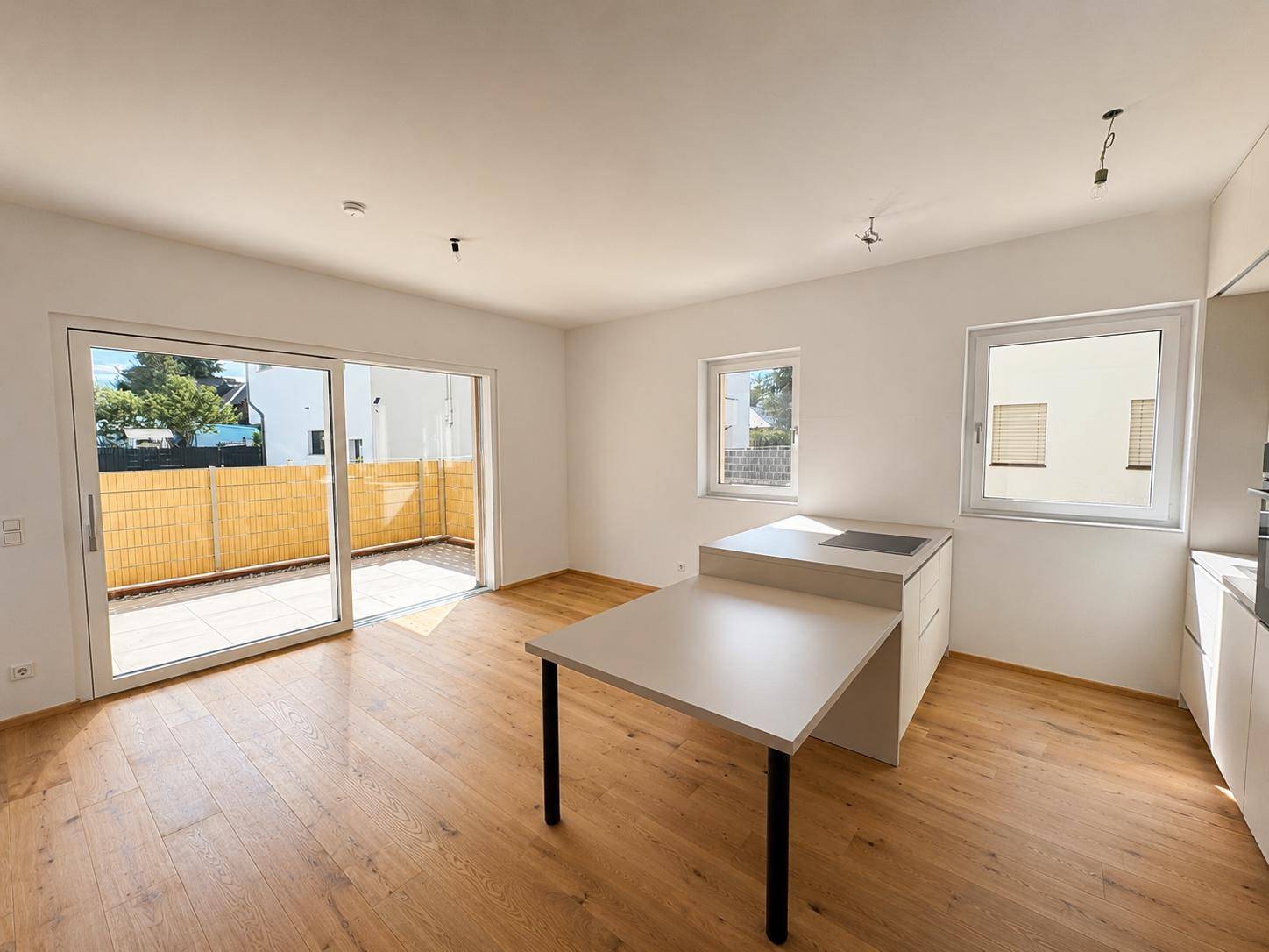 Lichtdurchfluteter Wohnbereich mit Holzboden, moderner Küchenzeile und direktem Zugang zur Terrasse.