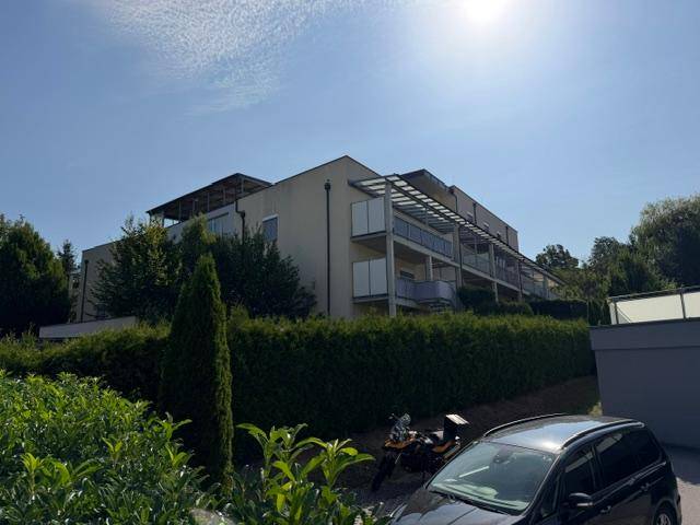 Modernes Wohngebäude mit Balkonen und gepflegter Hecke unter strahlendem Sonnenschein.