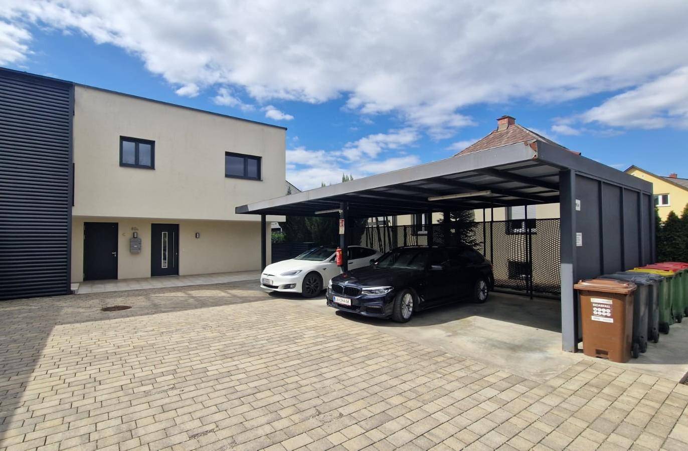 Gebäudefassade mit zwei überdachten Carports und ausreichend Parkmöglichkeiten.