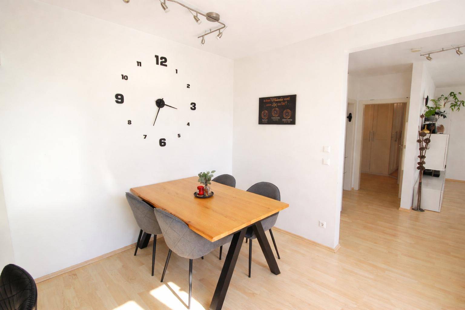 Gemütlicher Essbereich mit Holztisch, modernen Stühlen und dekorativer Wanduhr.