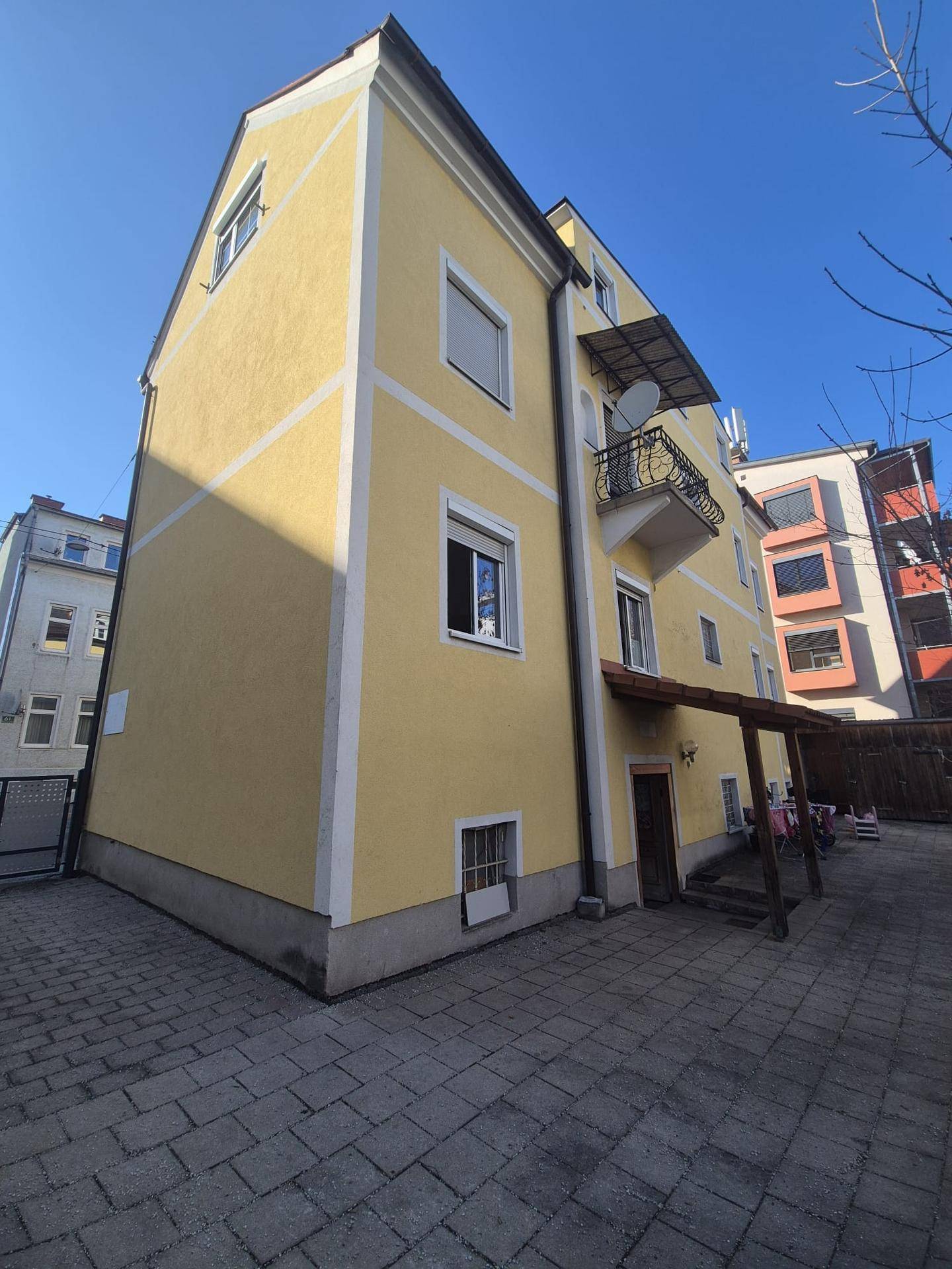 Seitenansicht des gelben Gebäudes mit kleinem Balkon und überdachtem Eingangsbereich.