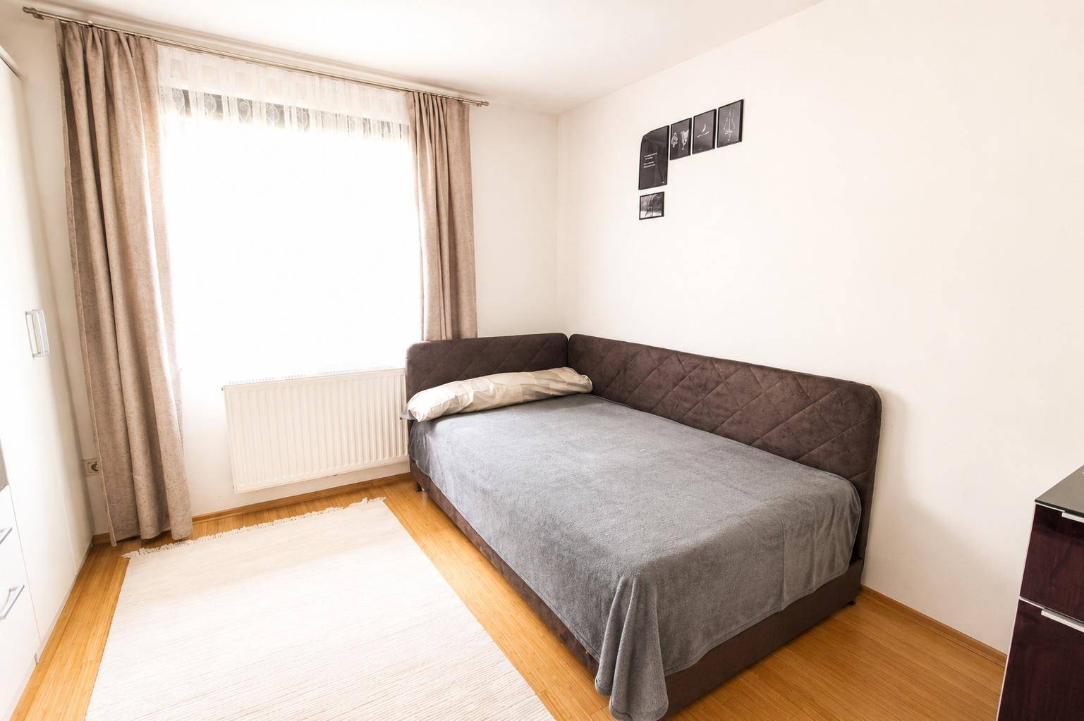 Weiteres Schlafzimmer mit Einzelbett, hellem Holzboden und großem Fenster mit Vorhängen.
