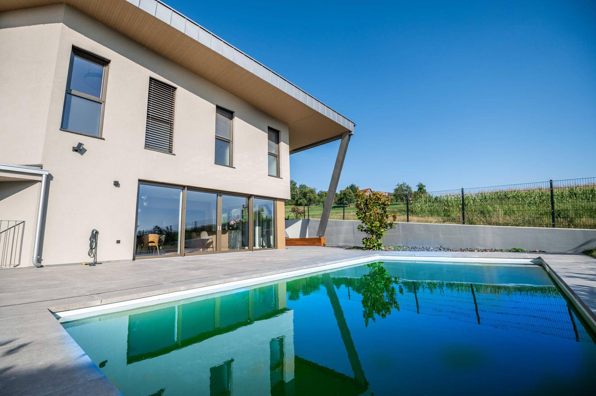 Moderne Villa mit großem Pool und weitläufiger Terrasse an einem sonnigen Tag.