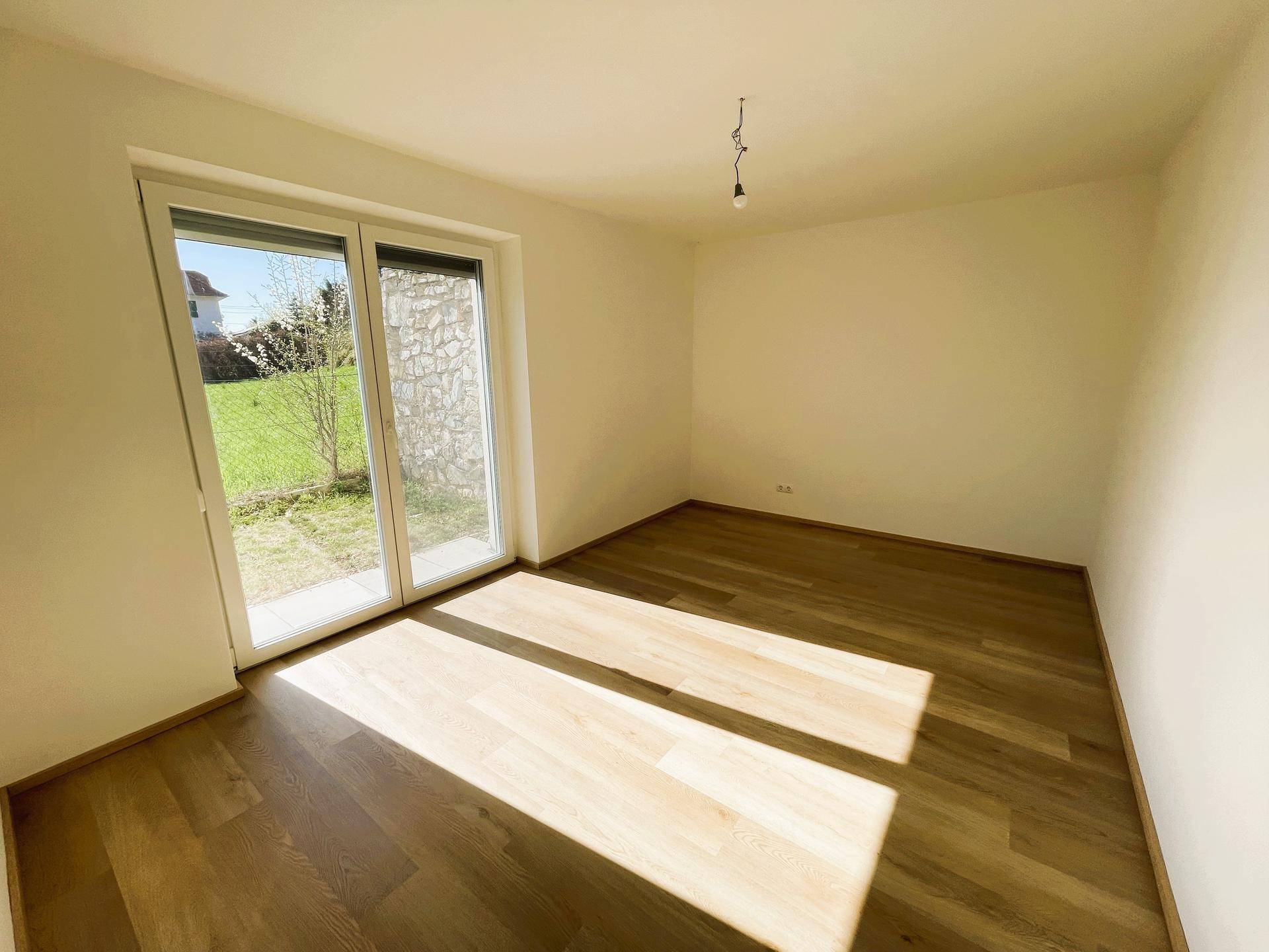 Helles Schlafzimmer mit Parkettboden und großem Fenster mit Blick ins Grüne.