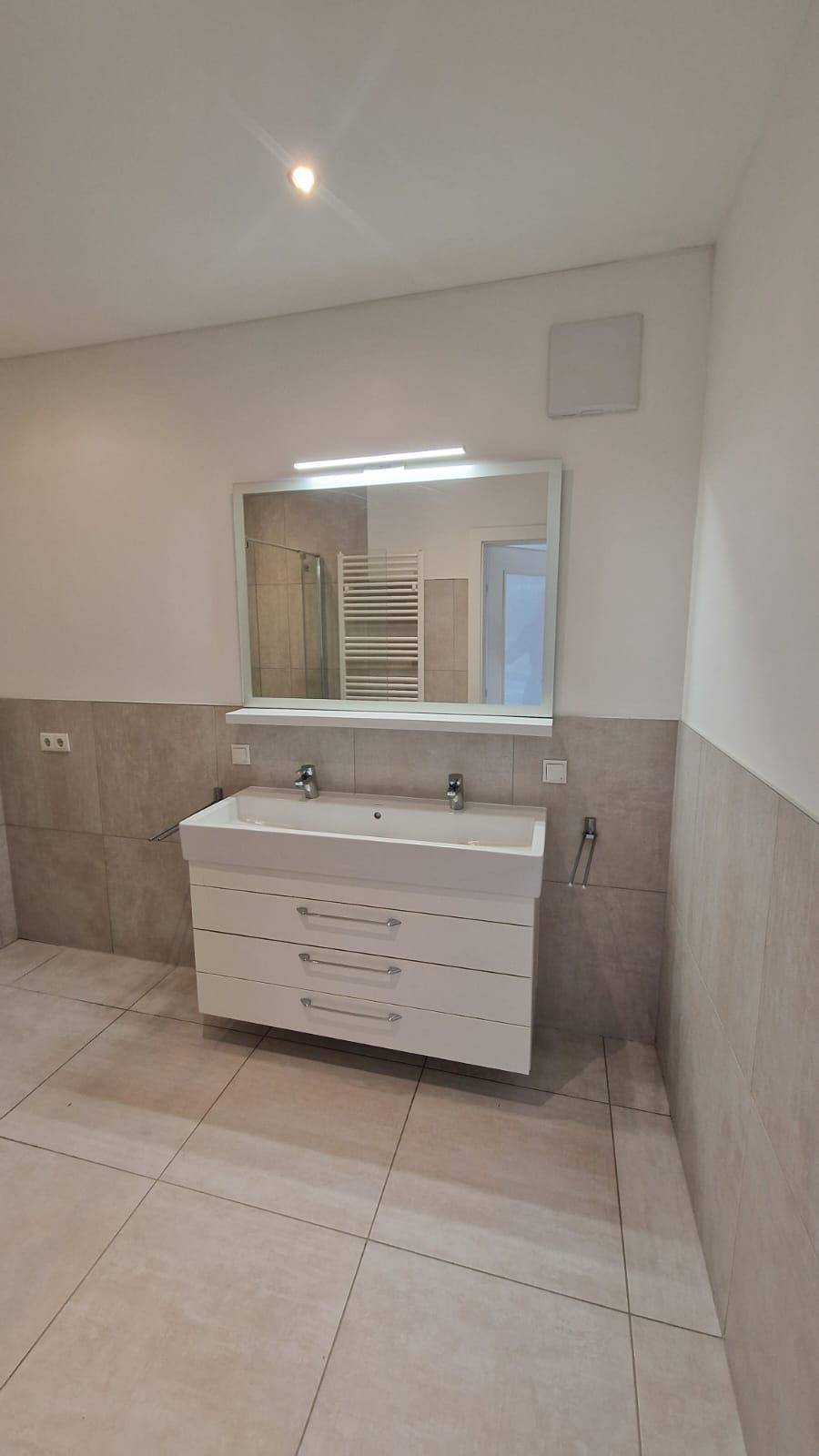 Helles Badezimmer mit Doppelwaschbecken, großem Spiegel und modernen Fliesen.
