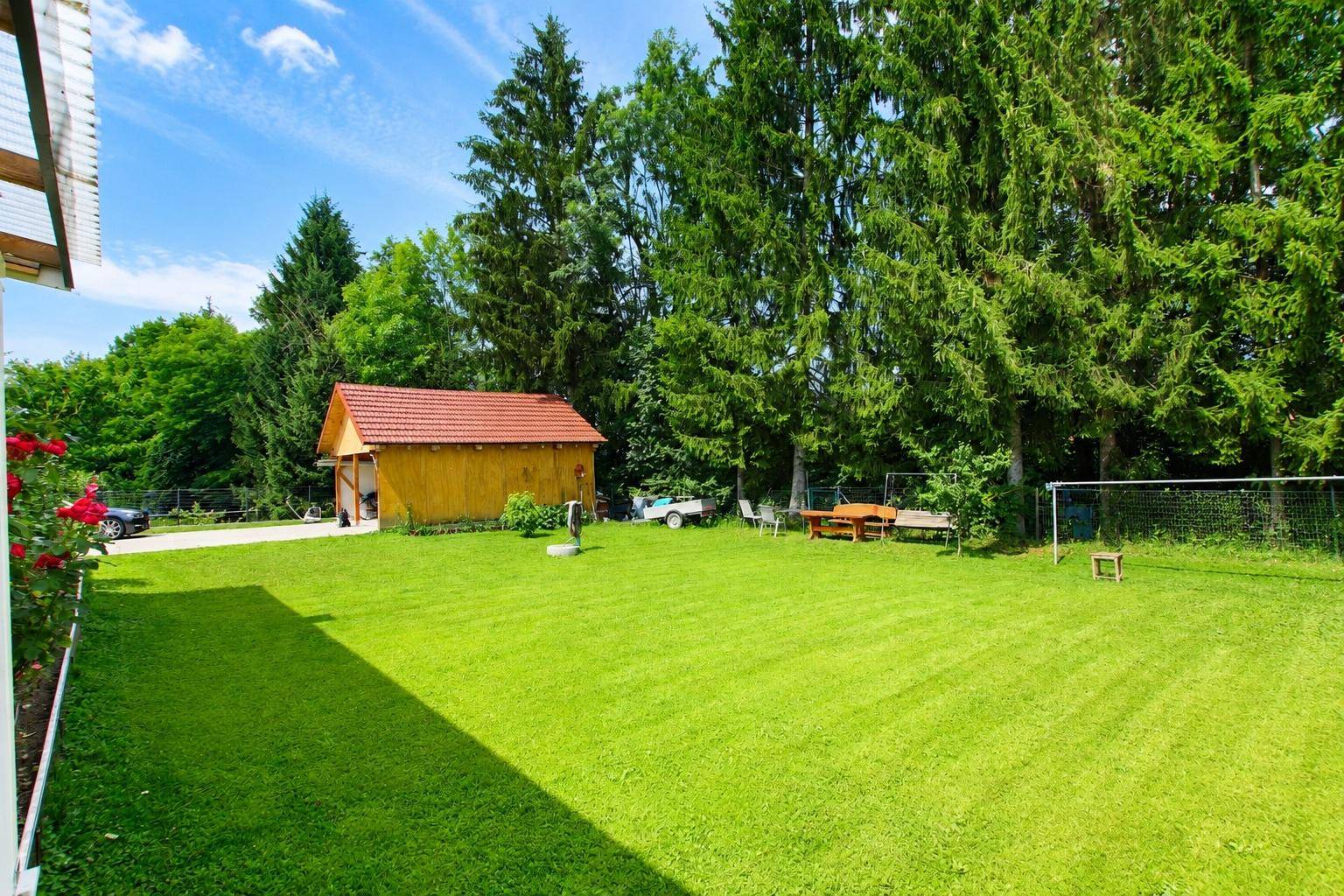 Gepflegter Garten mit großer Rasenfläche, Gartenhaus und Sitzgelegenheiten im Grünen.