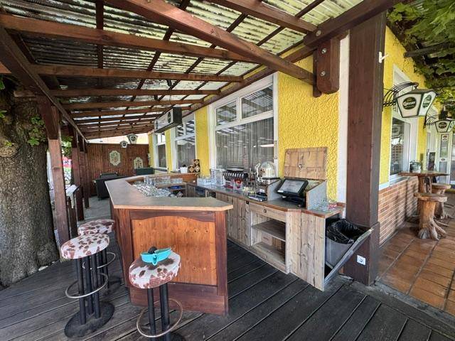Rustikale Außenbar auf einer Holzterrasse mit Überdachung und Hockern.