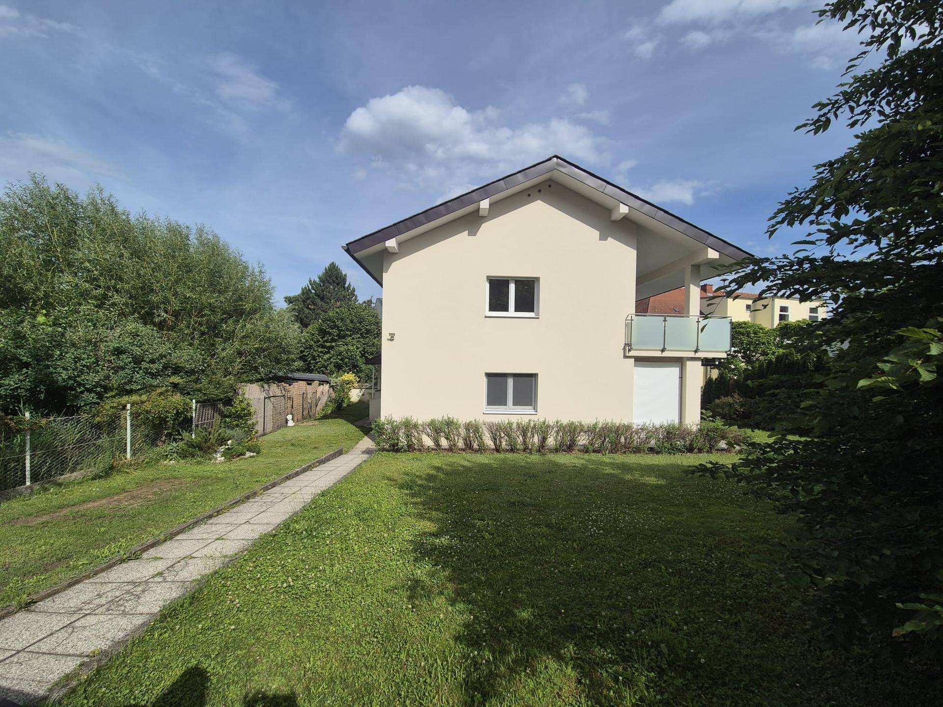Rückansicht des Hauses mit weitläufigem Garten und einem gepflasterten Weg.