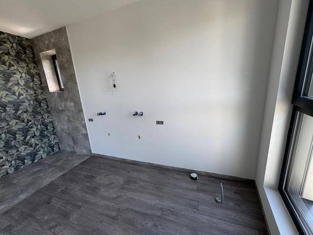 Unfertiges Badezimmer mit floraler Tapete, grauen Fliesen und Vorbereitung für Sanitärinstallationen.