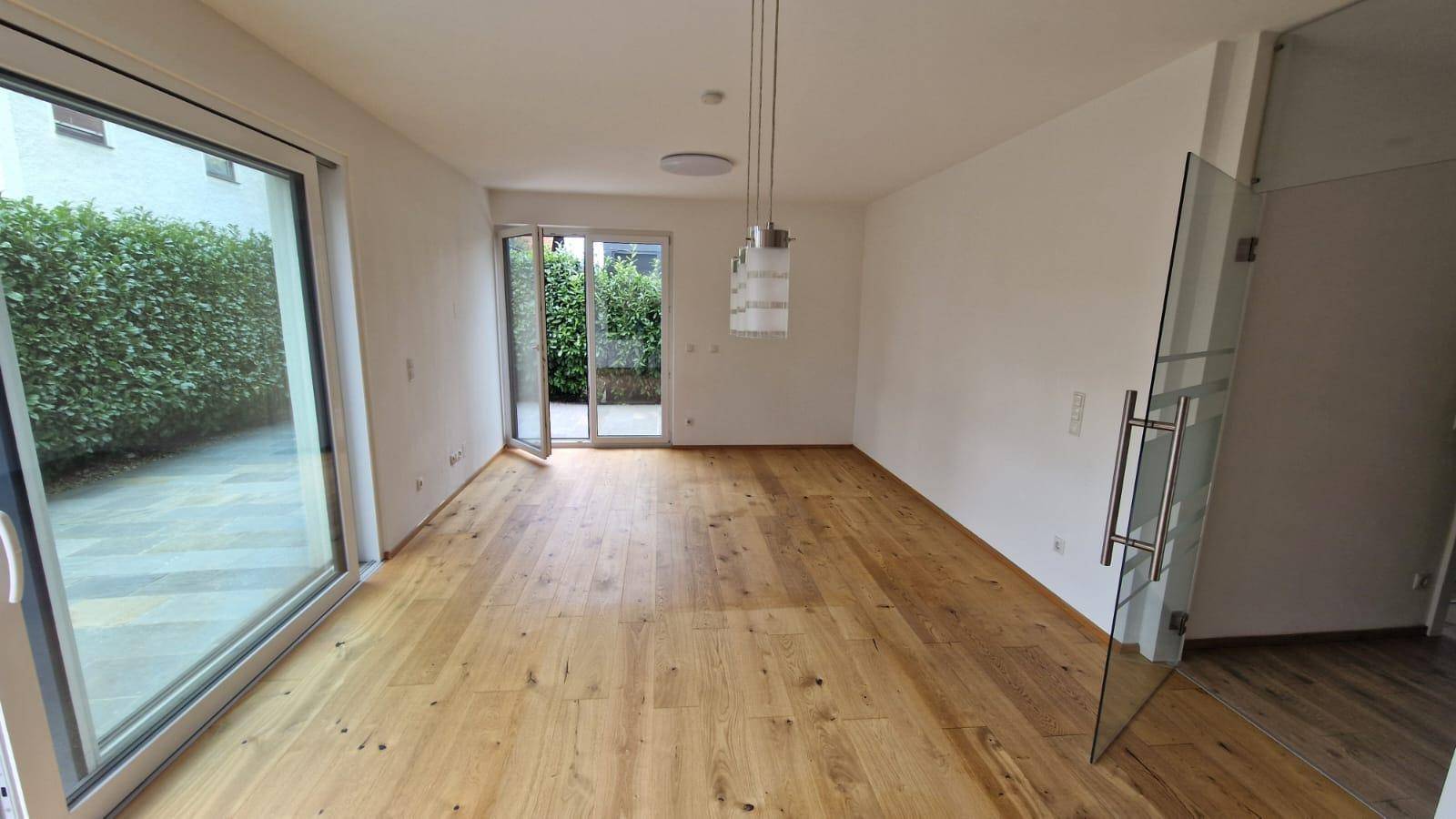 Geräumiger Wohnbereich mit Holzboden und viel Tageslicht durch große Fenster.