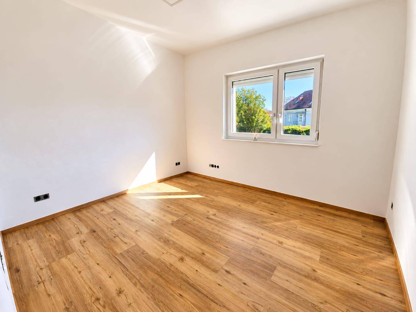 Helles Schlafzimmer mit Laminatboden und einem Fenster, das viel Tageslicht hereinlässt.