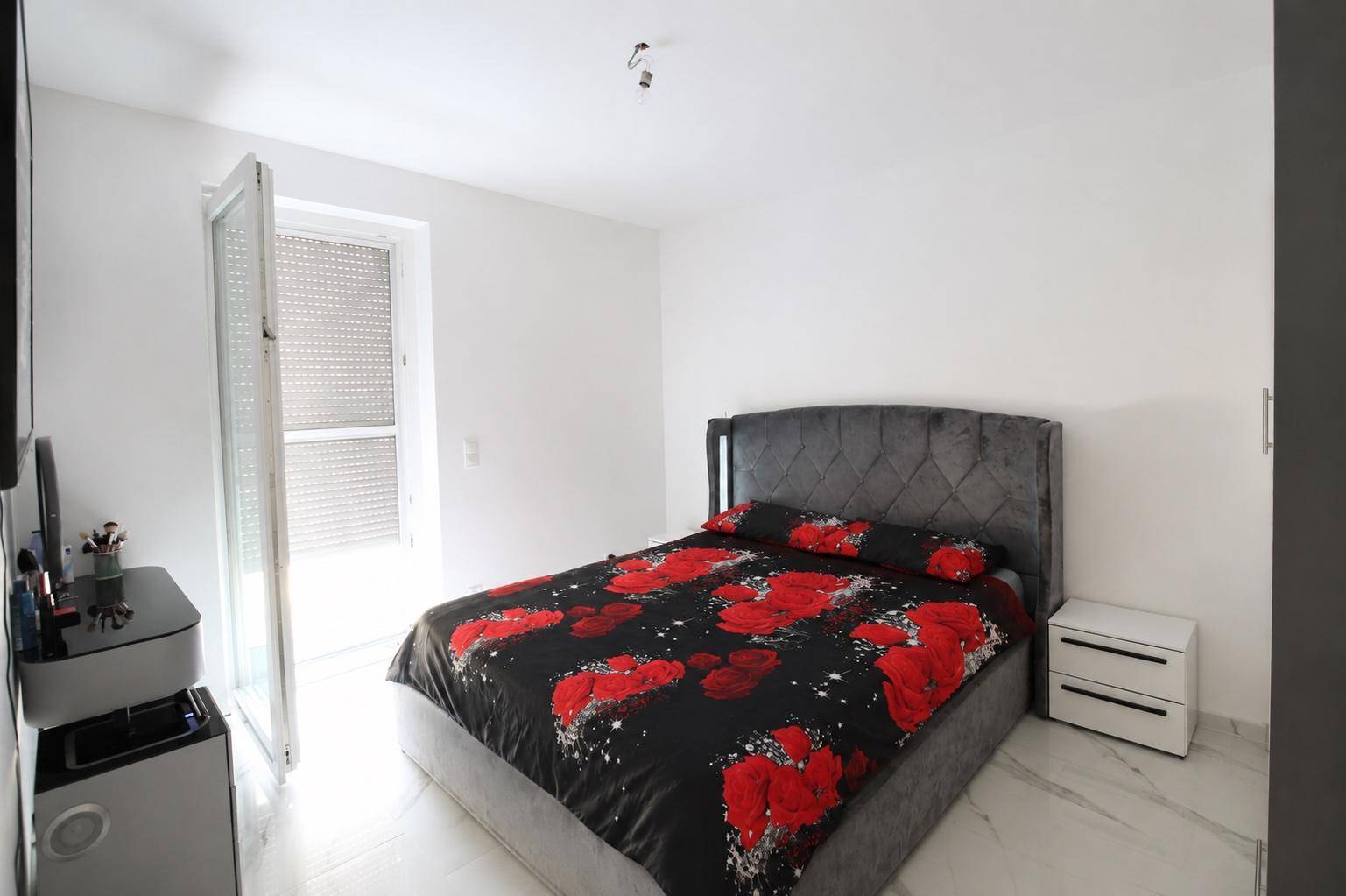 Schlafzimmer mit modernem Bett, floraler Bettwäsche und Zugang zum Außenbereich.