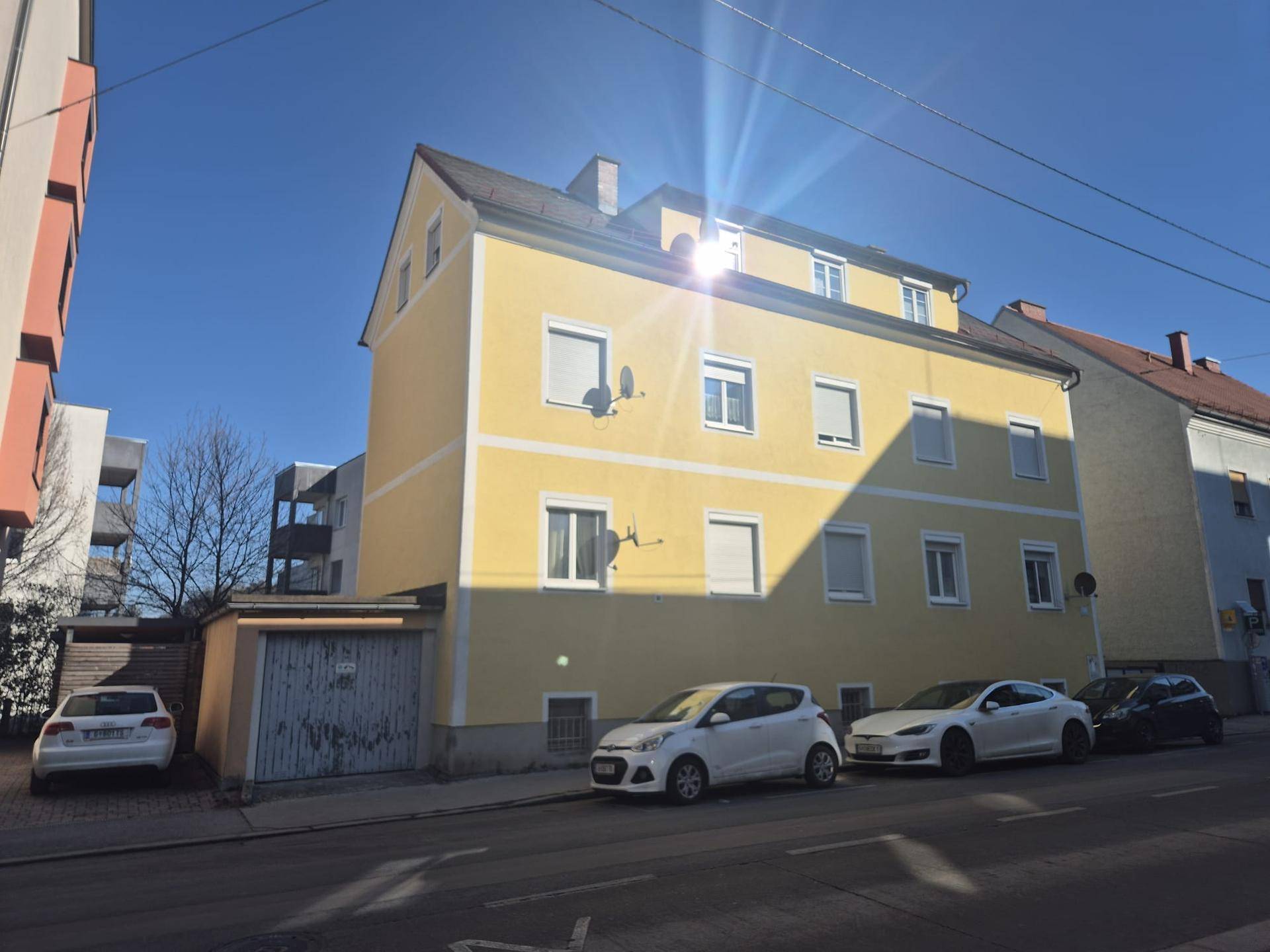 Gelbes Mehrfamilienhaus an einem sonnigen Tag von der Straße aus mit parkenden Autos.