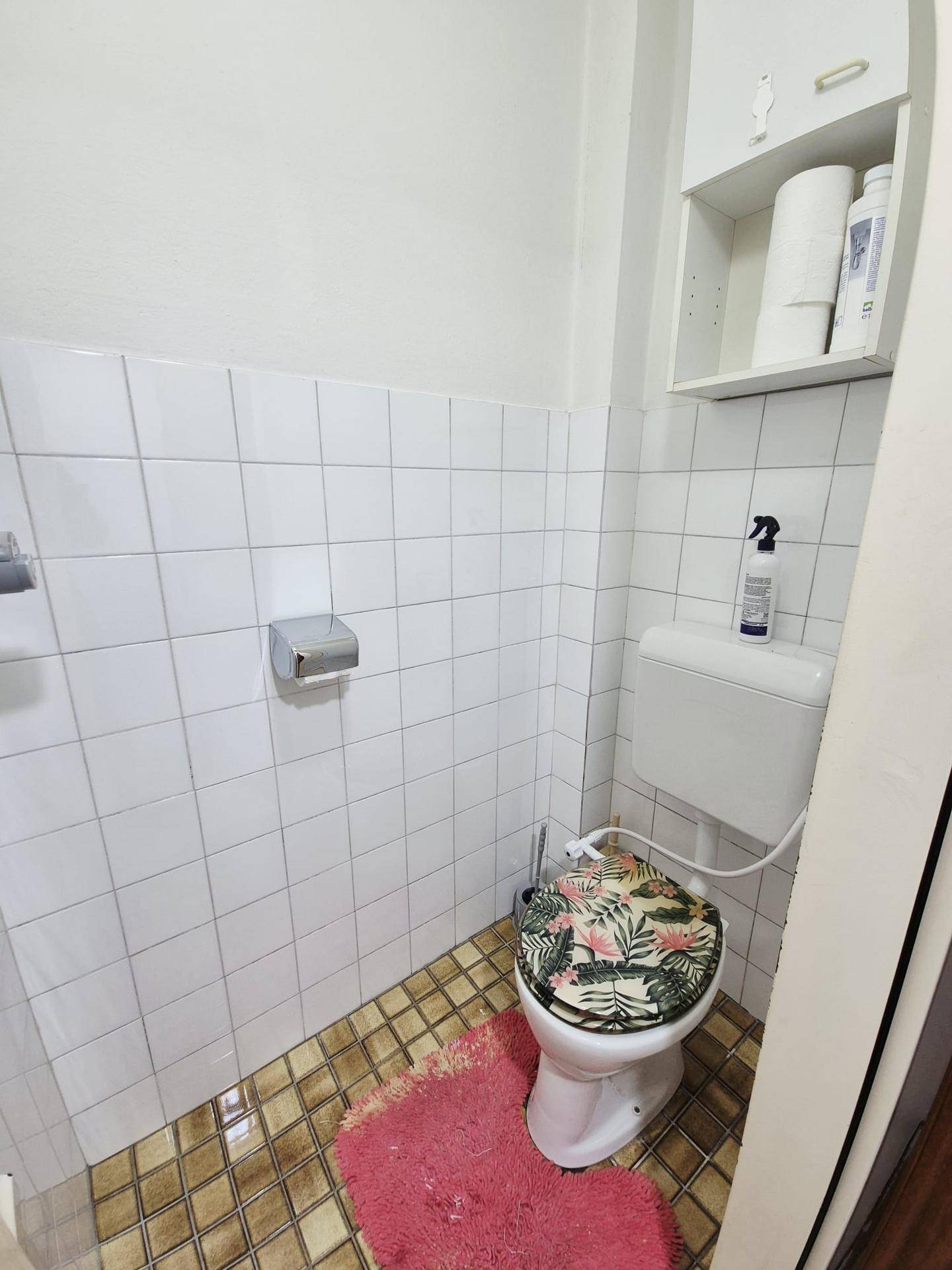 Separate Toilette mit weißen Fliesen und einem kleinen Regal.