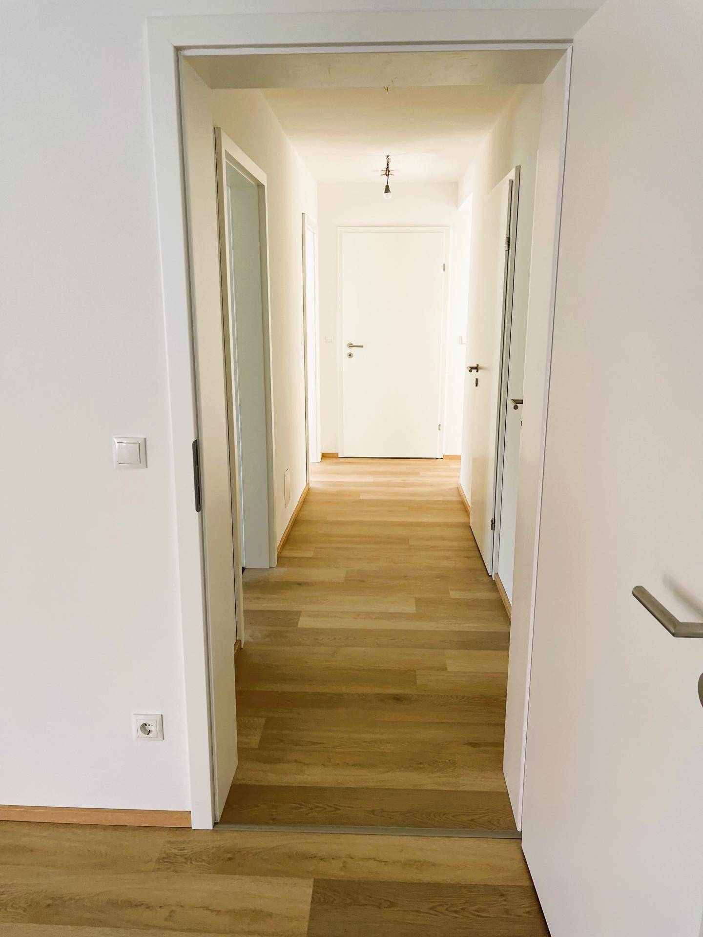 Heller Flur mit Holzfußboden und weißen Türen, der zu den verschiedenen Räumen führt.