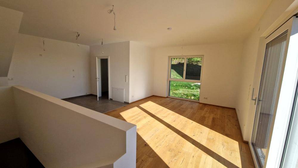 Heller Raum mit Holzboden und Fenster, das einen Blick auf die grüne Umgebung bietet.