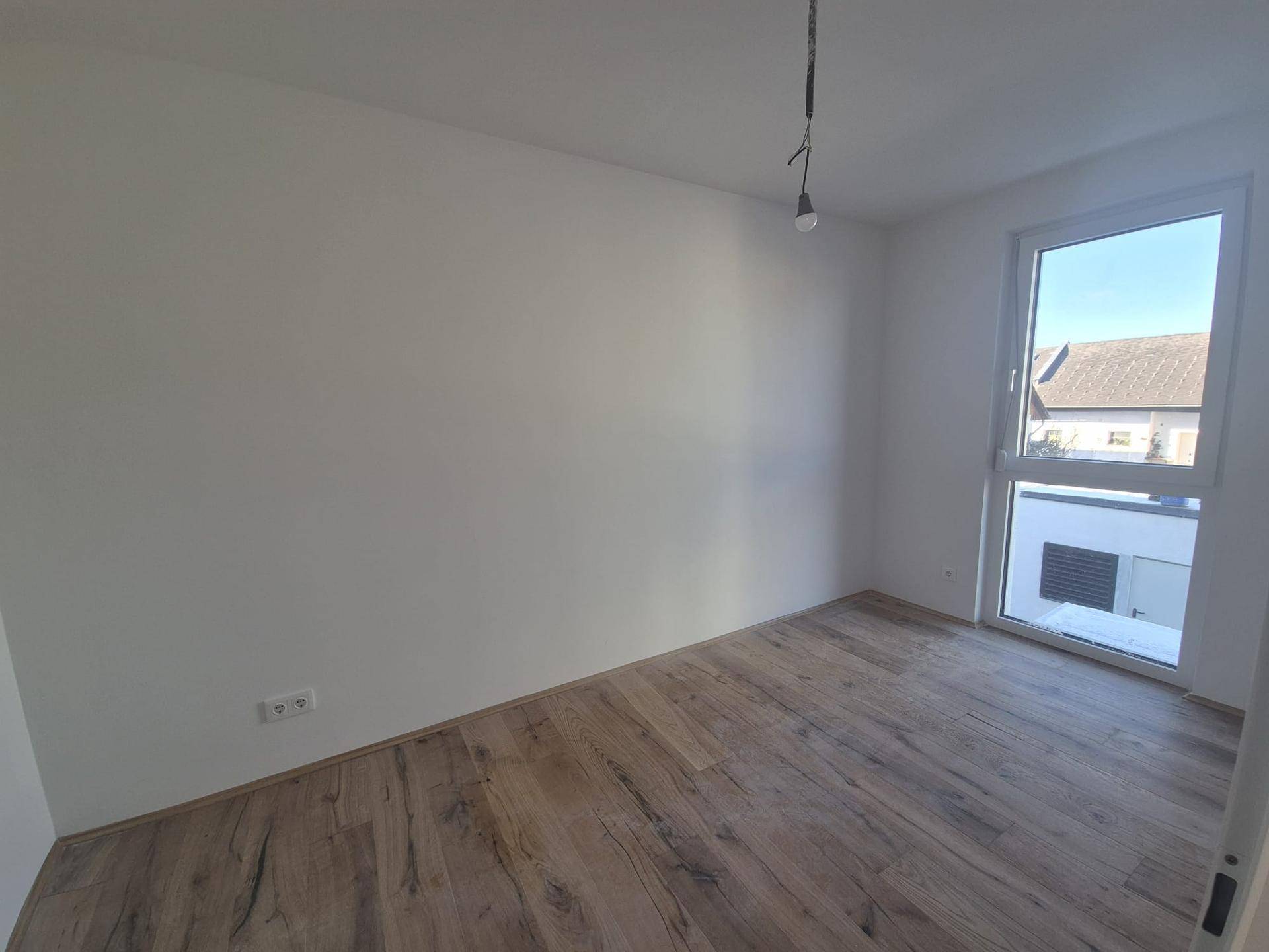 Geräumiges Zimmer mit hellem Holzboden und Fenster, bietet vielseitige Nutzungsmöglichkeiten.