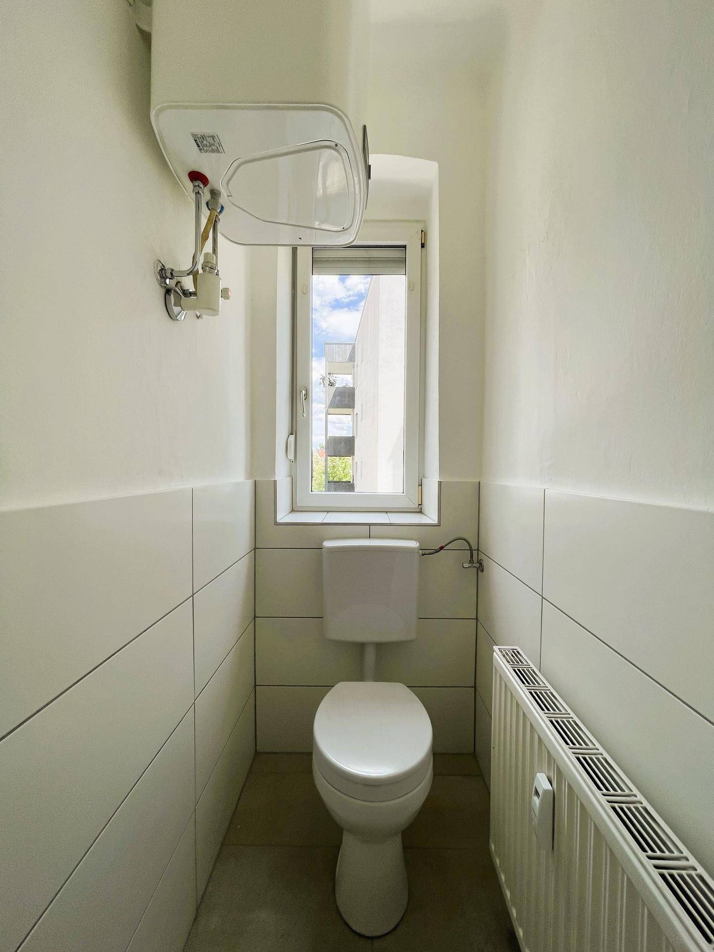 Modernes Gäste-WC mit Fenster, weiß gefliesten Wänden und einem wandmontierten WC.