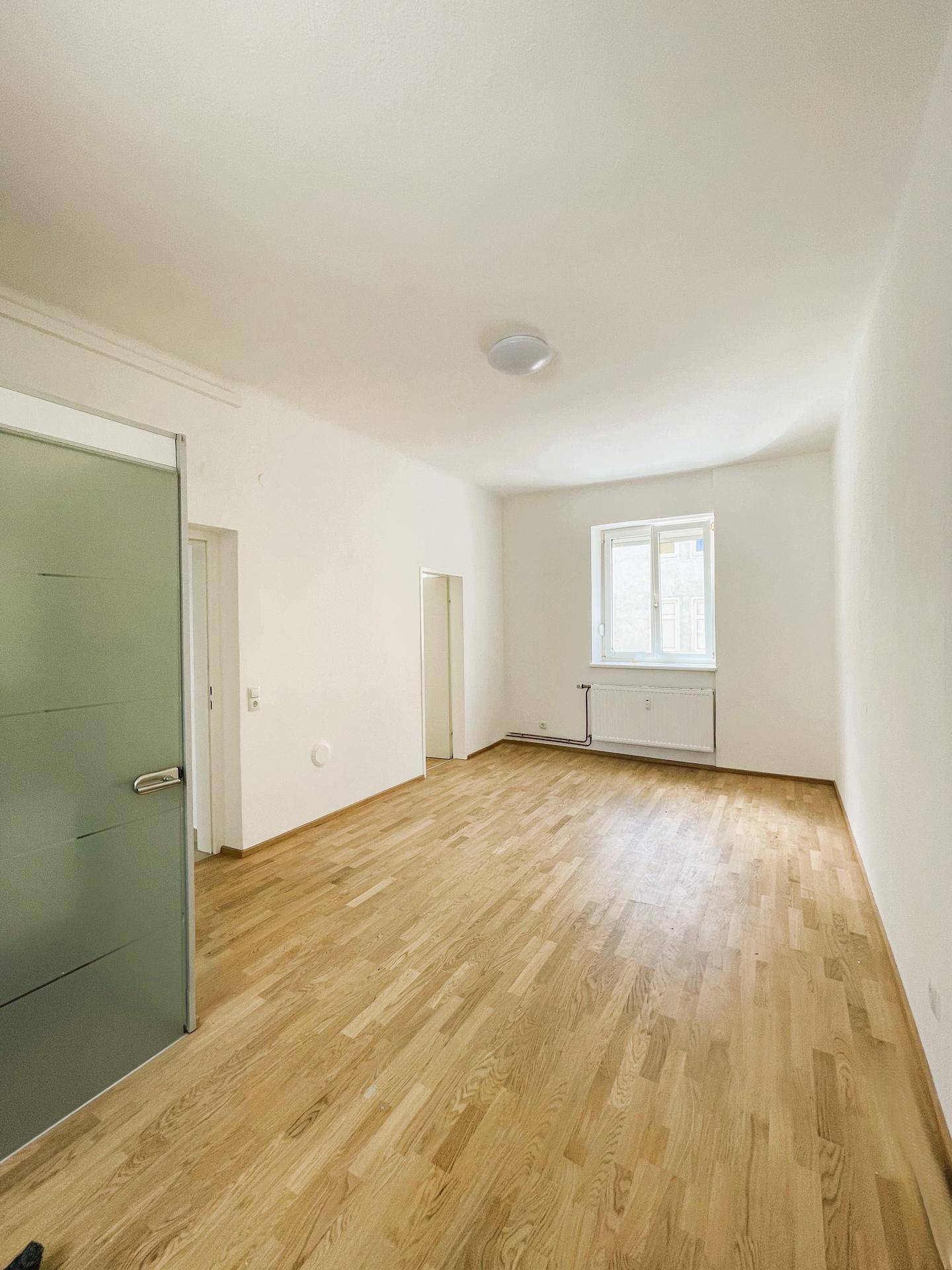 Helles, modernisiertes Zimmer mit Parkettboden, weißen Wänden und einem Fenster, das viel Tageslicht hereinlässt.