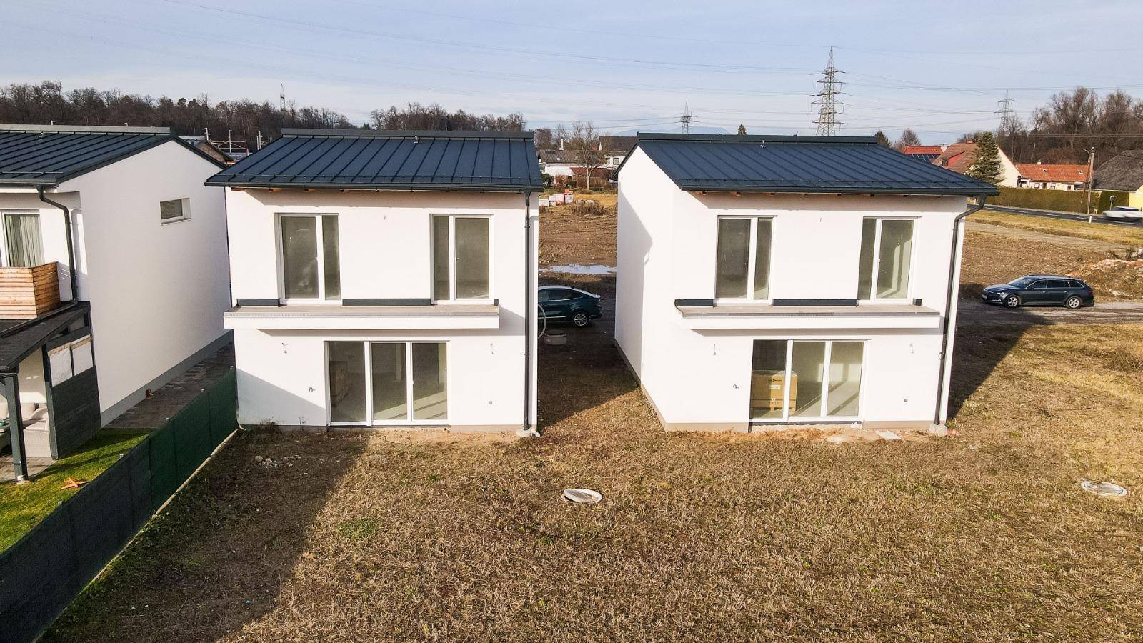 Draufsicht auf zwei moderne Neubauten mit dunklen Dächern und weißer Fassade in offener Landschaft.