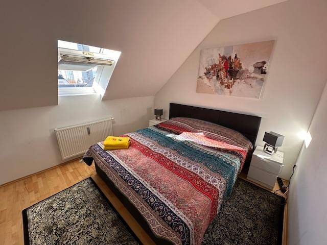 Helles Schlafzimmer im Dachgeschoss mit Holzboden, Dachfenster und moderner Kunst an der Wand.