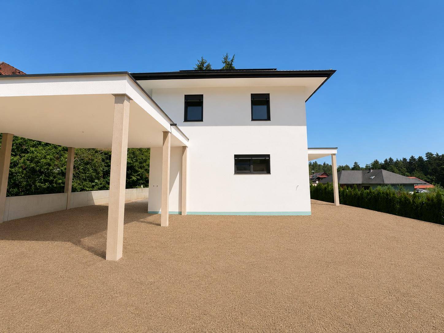 Seitenansicht des modernen Einfamilienhauses mit Carport und großer Kiesfläche.