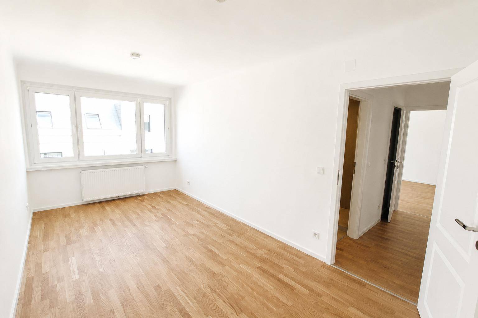 Lichtdurchflutetes Schlafzimmer mit hellem Parkettboden und Blick nach draußen durch die Fenster.