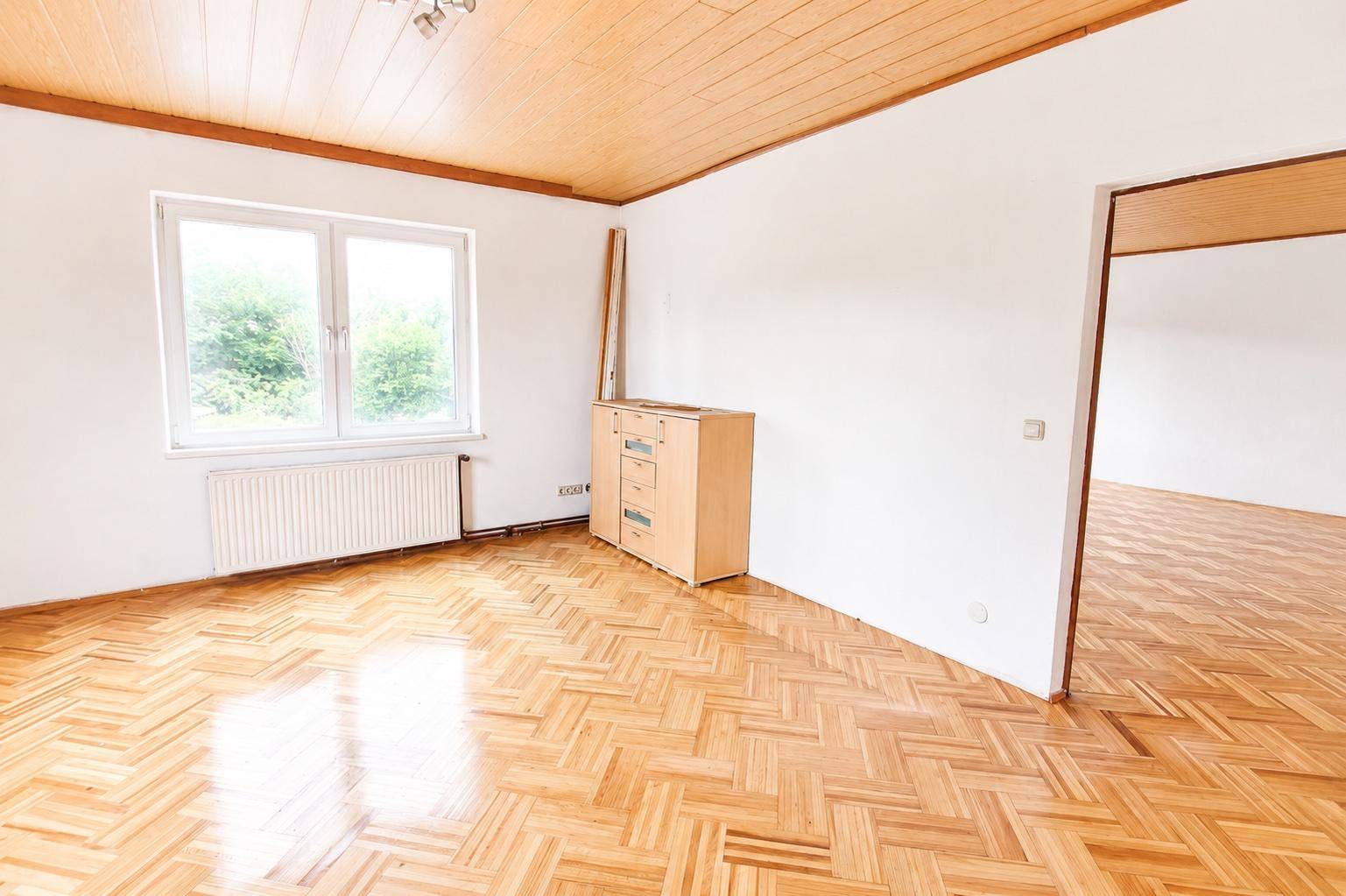 Leerer Raum mit glänzendem Holzparkettboden, weißen Wänden und einem Fenster.