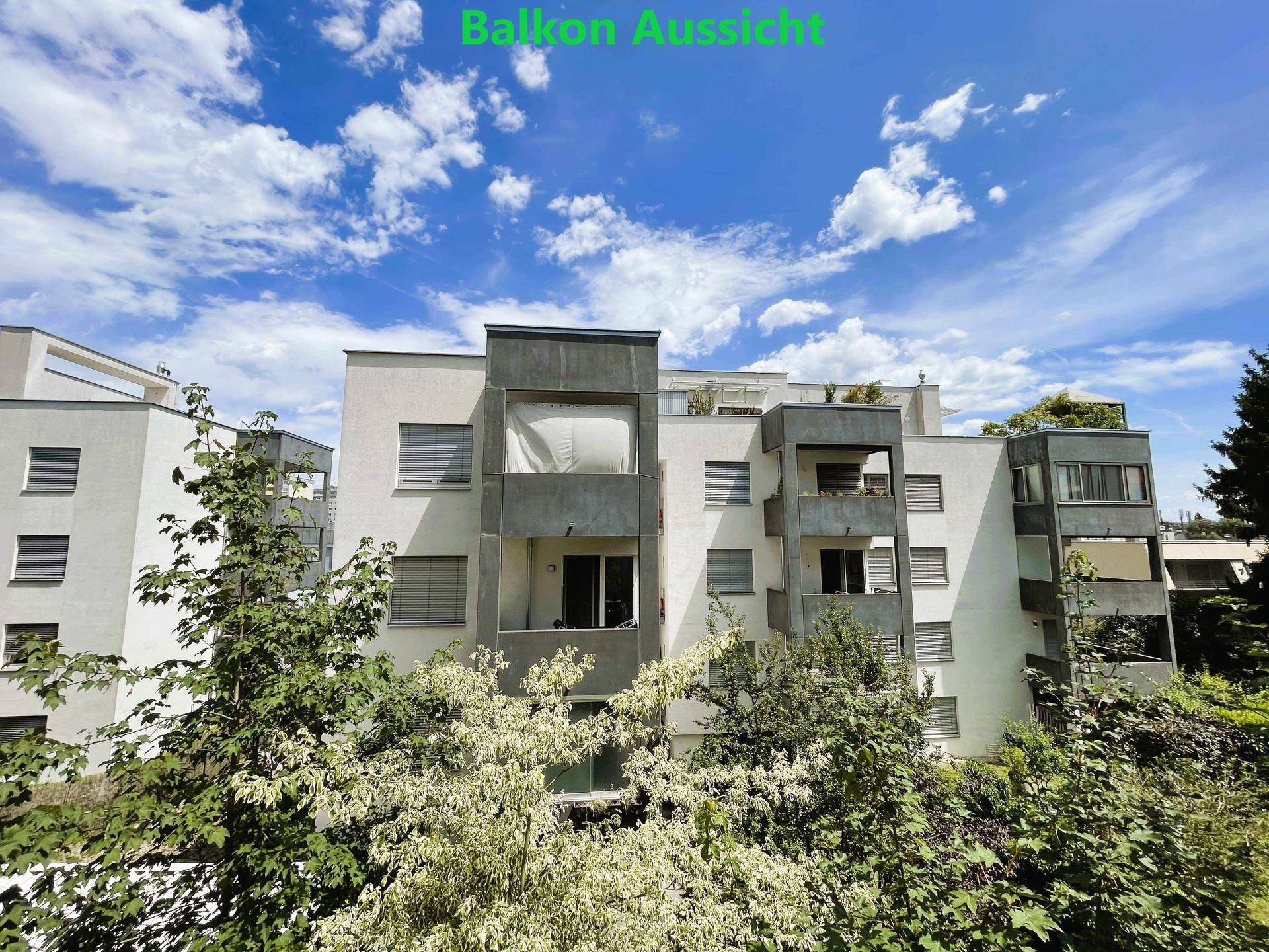 Blick auf ein modernes Mehrfamilienhaus mit viel Grün und Bäumen im Vordergrund.