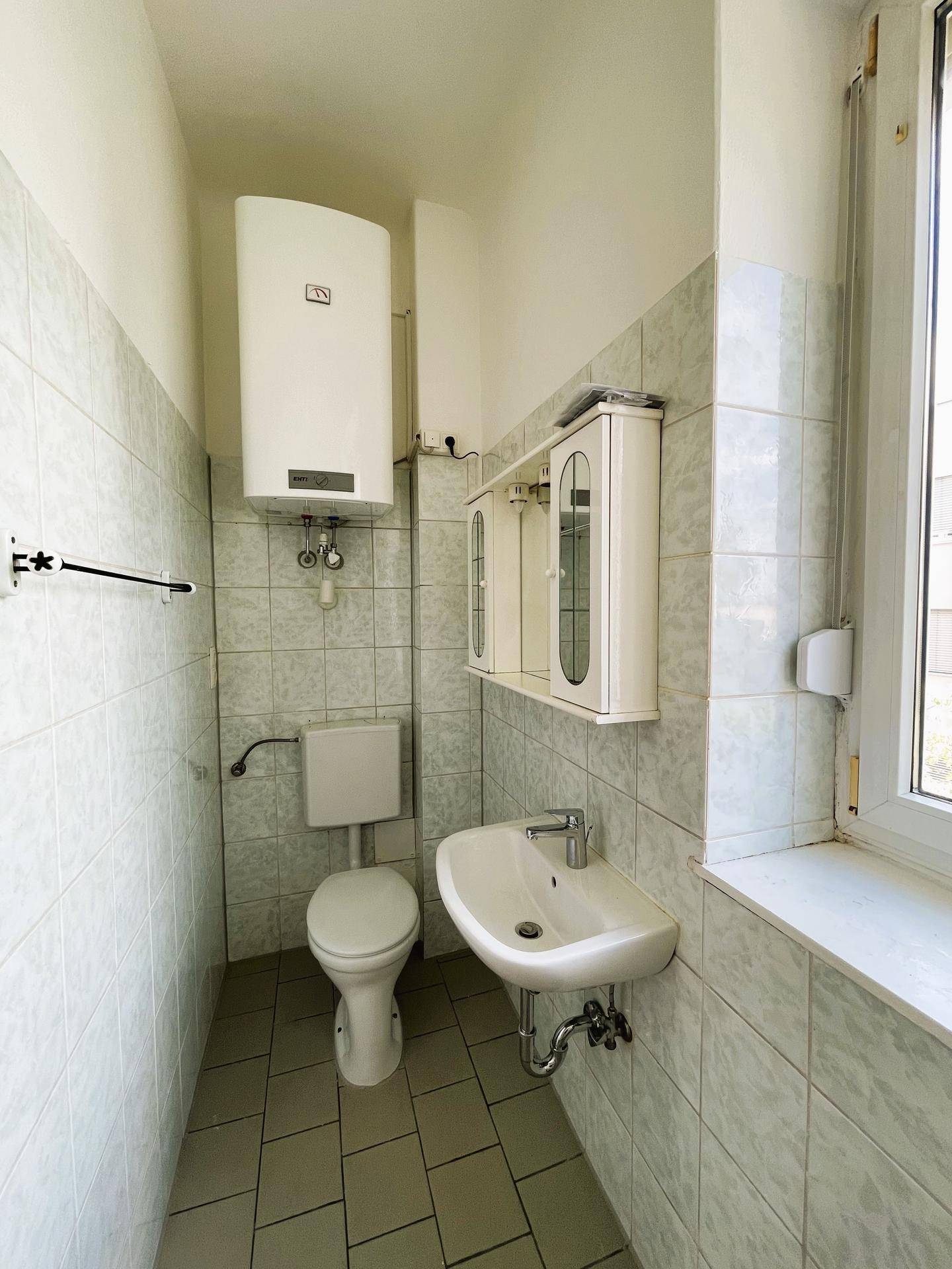 Kleines Badezimmer mit WC, Waschbecken, Spiegelschrank und Fenster, hell gefliest.