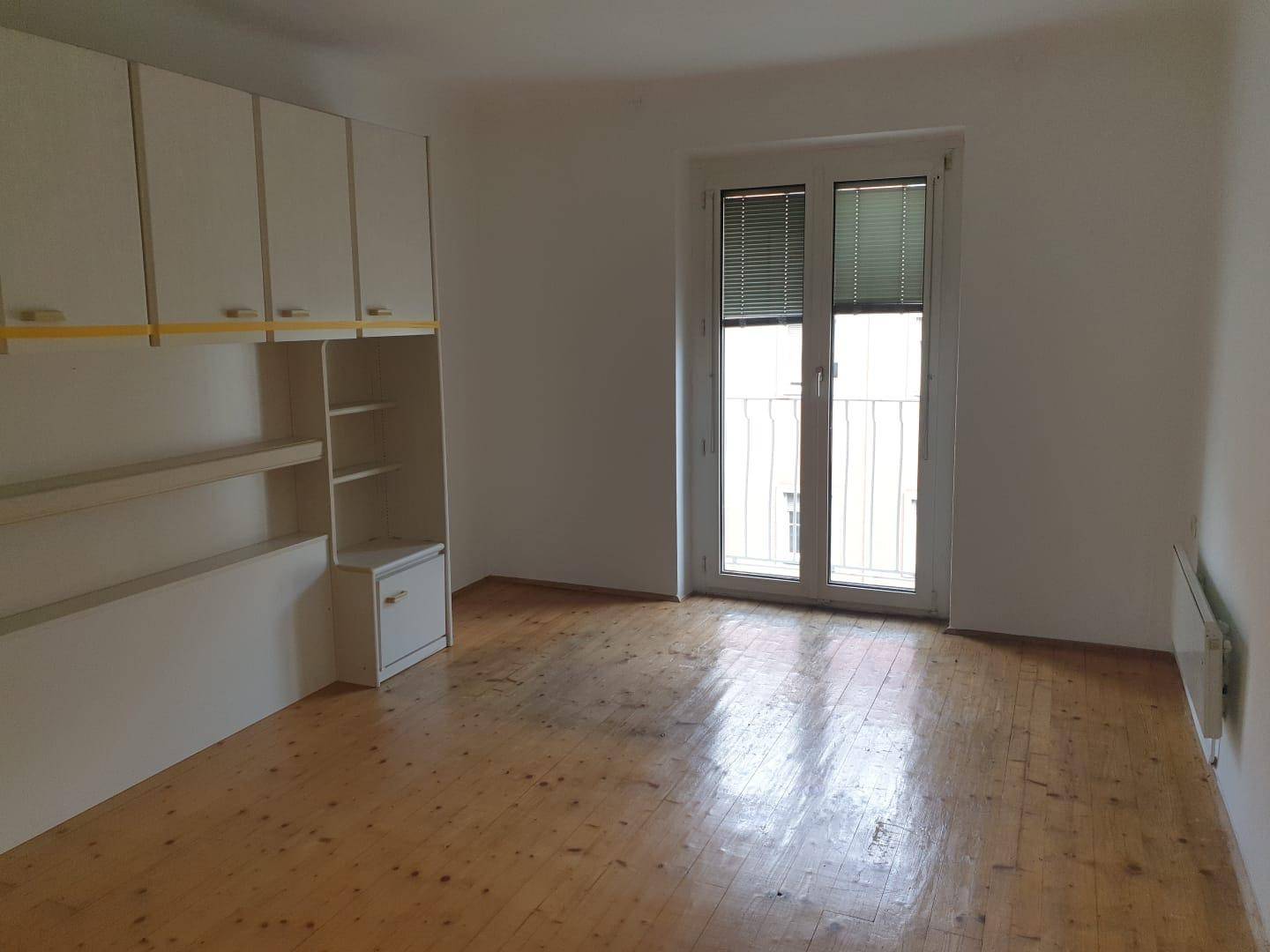 Helles Zimmer mit Holzdielenboden, Einbauschränken und einer Fenstertür zu einem französischen Balkon.