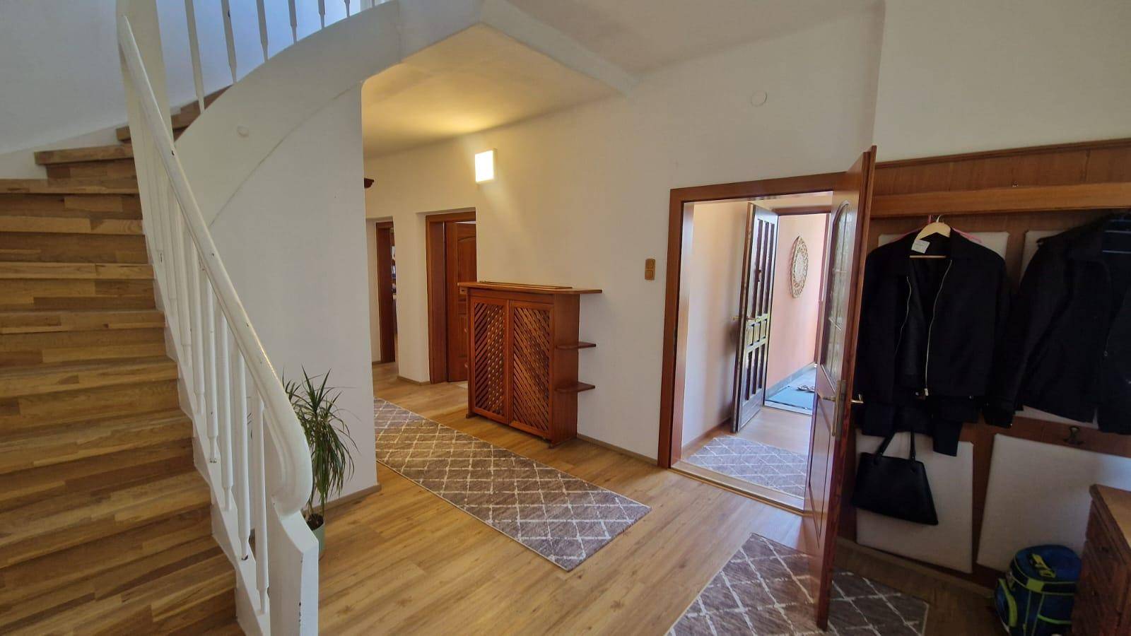 Geräumiger Flur mit Holztreppe, Laminatboden und Garderobe, der verschiedene Bereiche verbindet.