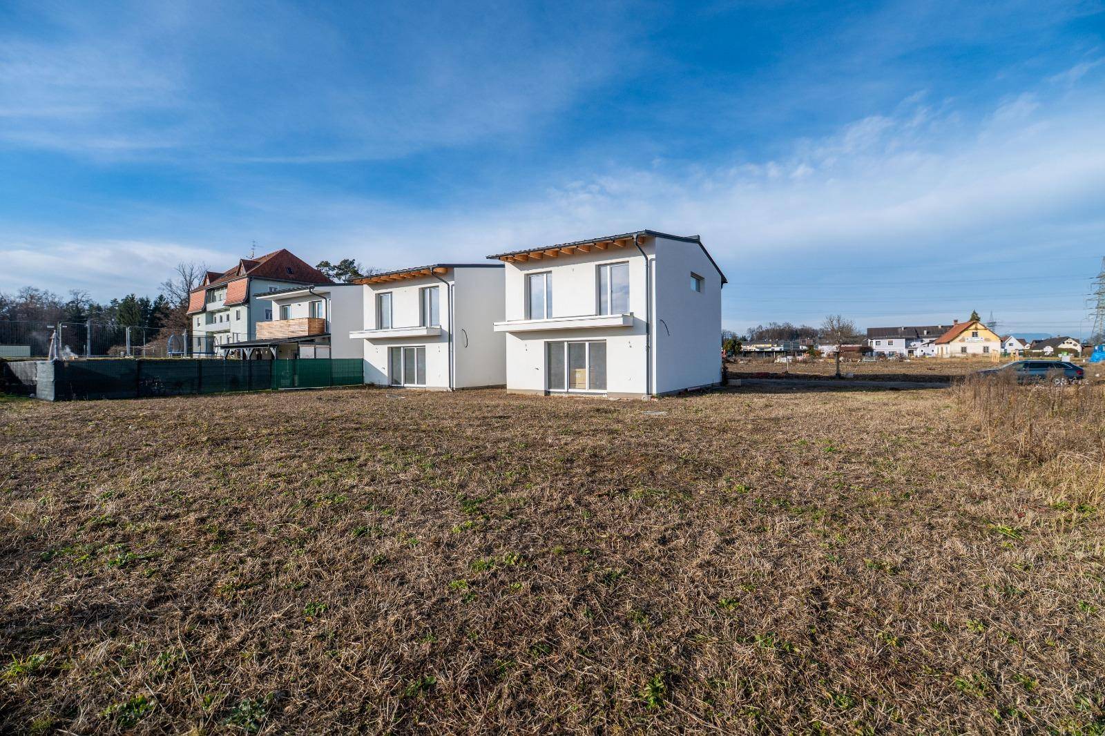 Zwei moderne Neubauten mit weißer Fassade und dunklem Dach in ländlicher Umgebung.