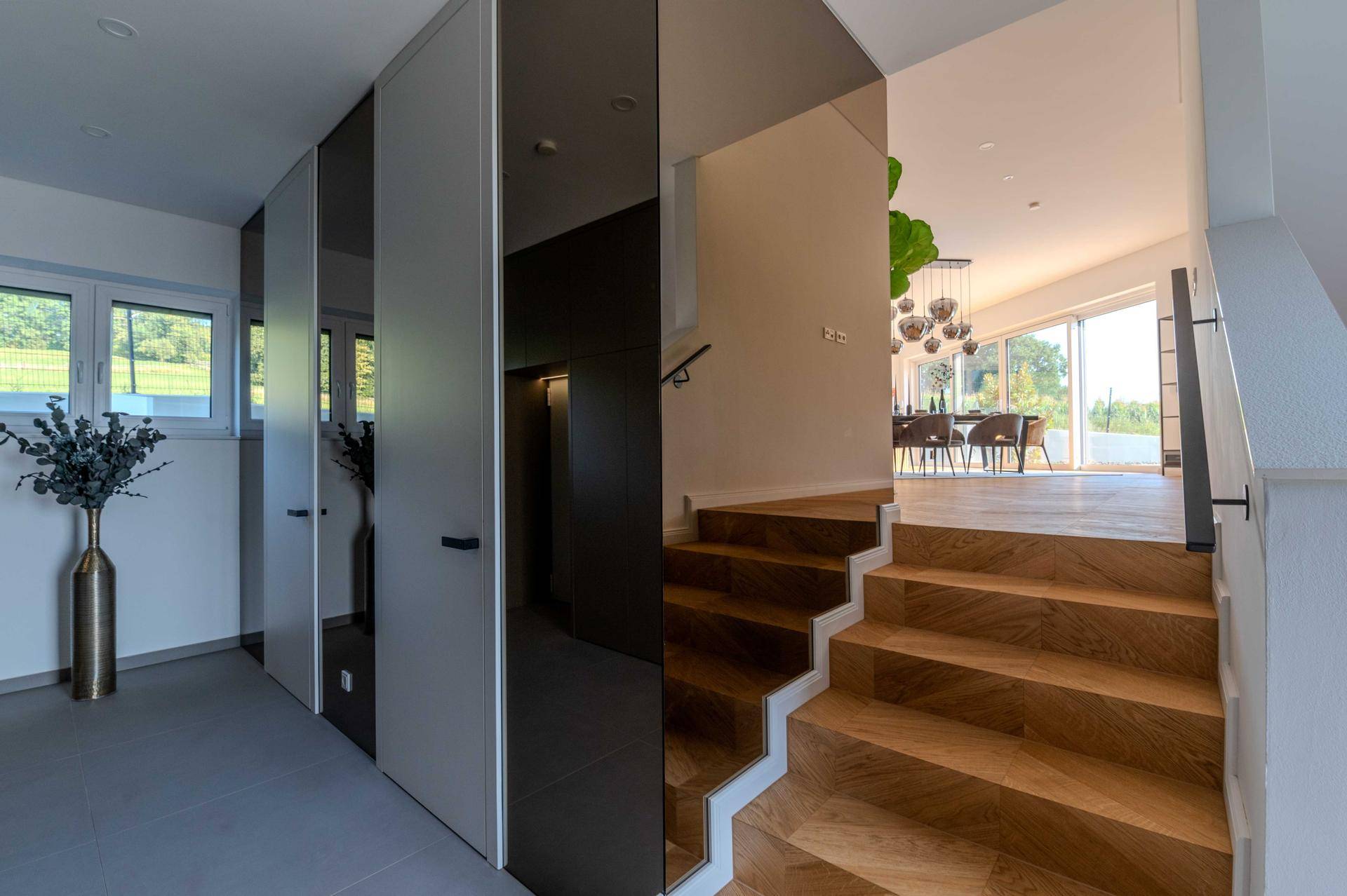 Heller Eingangsbereich mit Holztreppe und Blick in den offenen Wohn-Essbereich.