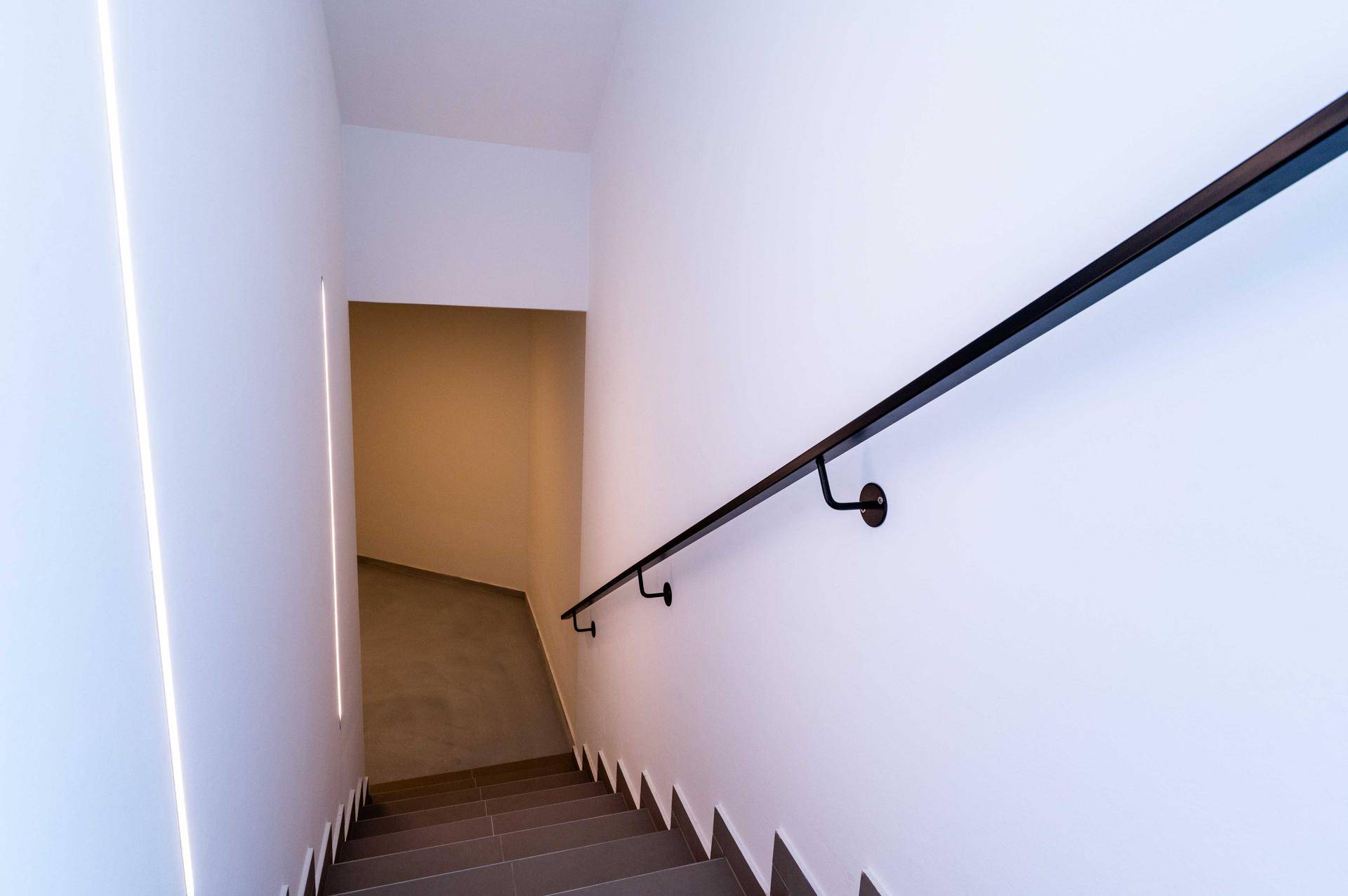 Treppenabgang in den Keller mit moderner Beleuchtung und Handlauf.