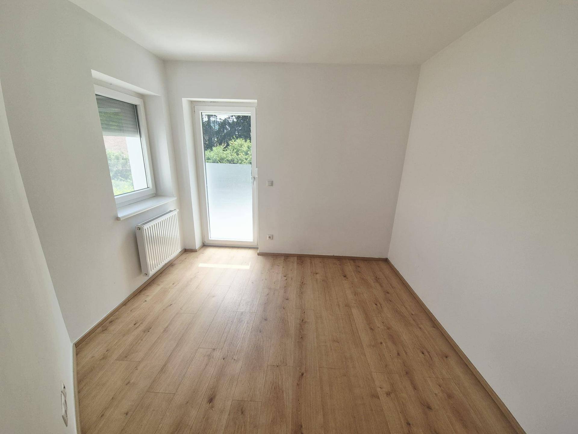 Helles Schlafzimmer mit modernem Laminatboden, weißen Wänden und Zugang nach draußen.