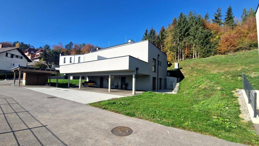 Modernes Gebäude mit Carport und grüner Umgebung, eingebettet in eine natürliche Landschaft.