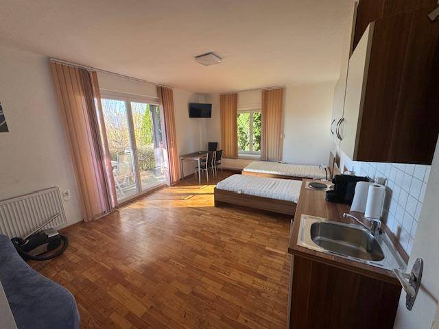Helles Studio-Apartment mit Holzboden, zwei Betten, kleiner Küchenzeile und Zugang zur Terrasse.