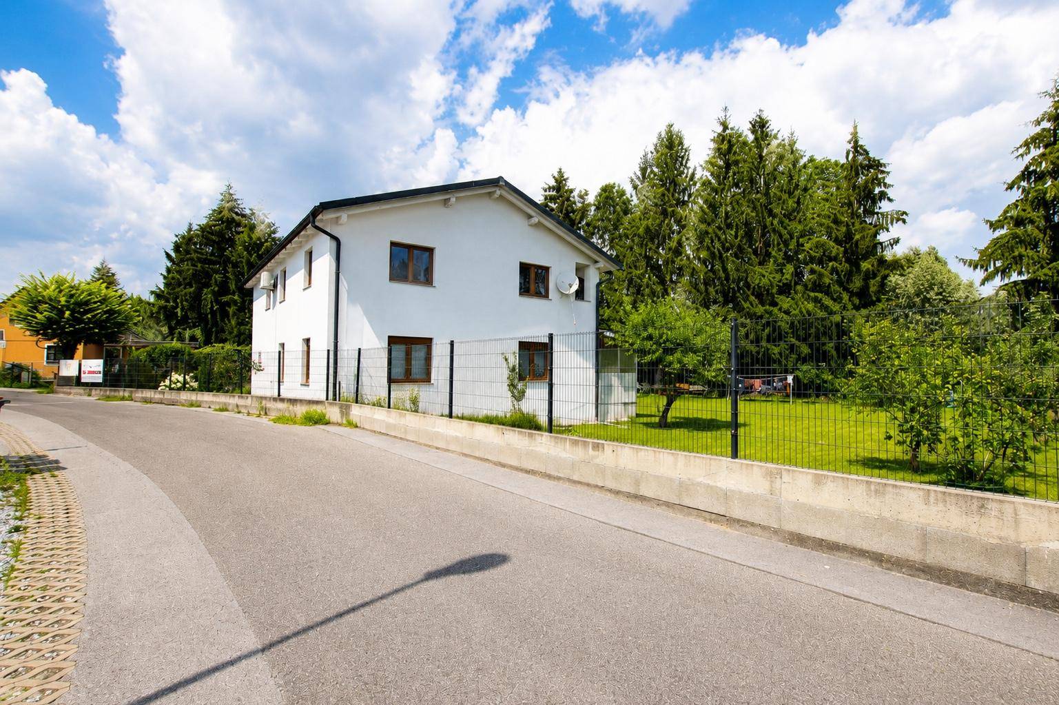 Seitenansicht des modernen Einfamilienhauses von der Straße mit umzäuntem Gartenbereich.