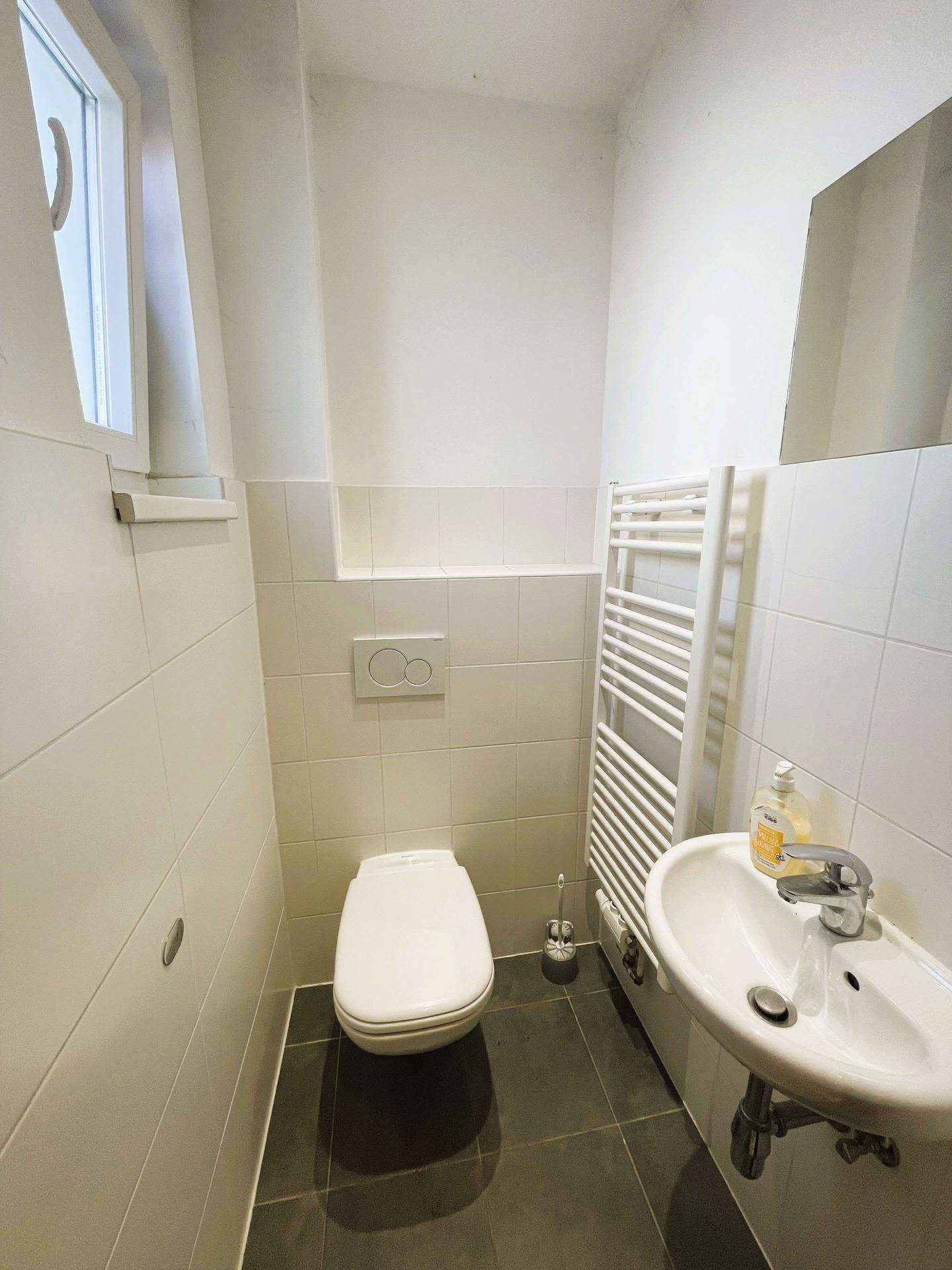 Kleines Gäste-WC mit Fenster, Waschbecken und Wand-WC, in schlichtem Design.