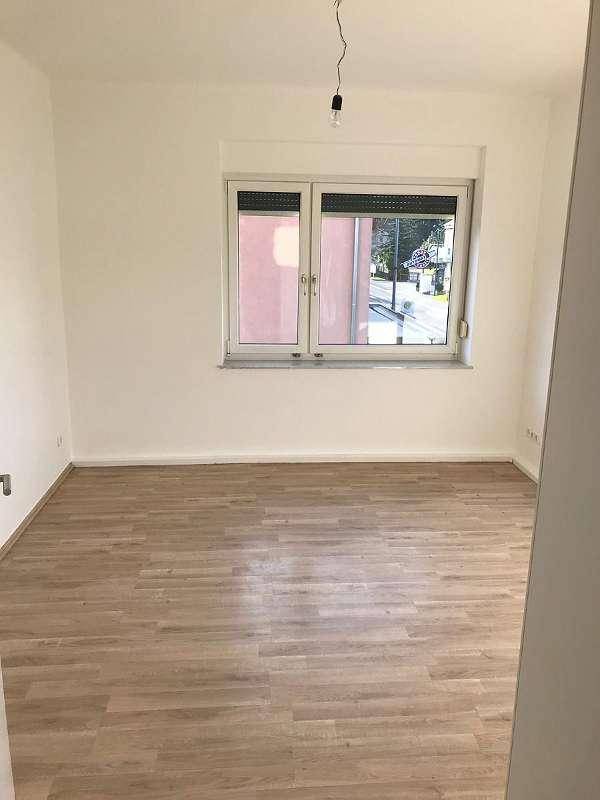 Leeres Zimmer mit hellem Laminatboden, weißen Wänden und einem Fenster mit Blick nach draußen.