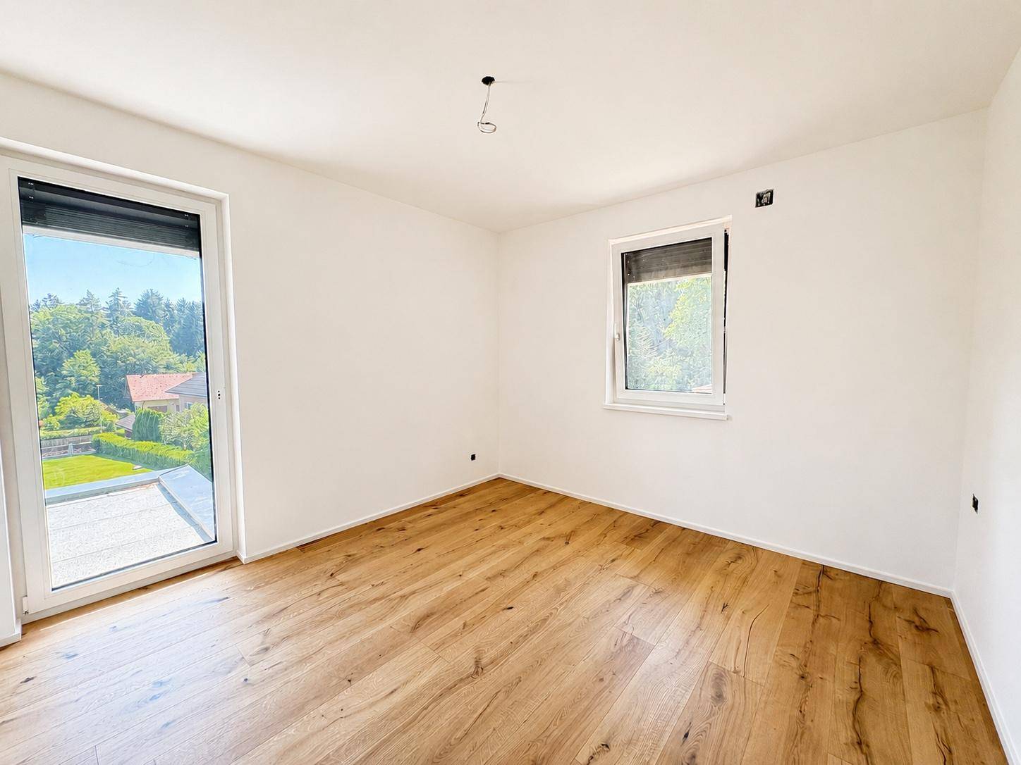 Schlafzimmer mit hellem Parkettboden, großen Fenstern und Zugang zu einem Balkon oder einer Terrasse.