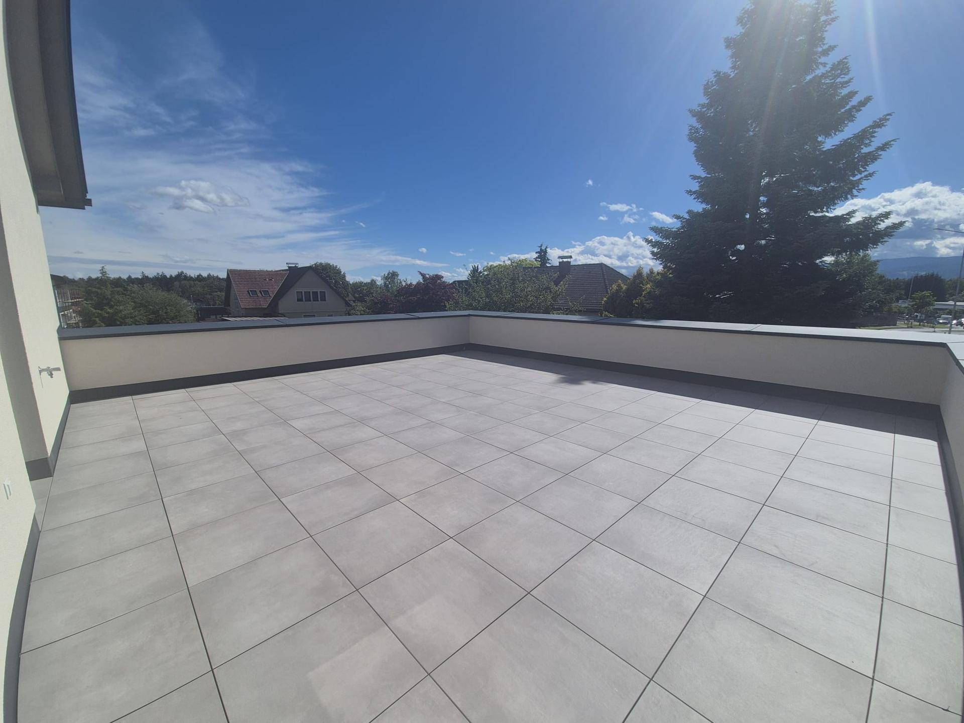 Geräumige Dachterrasse mit modernen Fliesen und einem weiten Blick unter blauem Himmel.