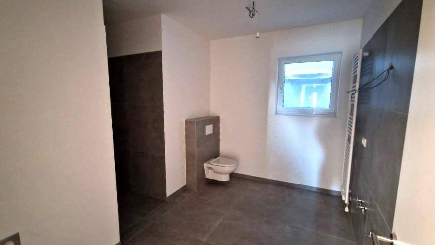 Modernes Badezimmer mit dunklen Fliesen, wandhängendem WC und Fenster für Tageslicht.