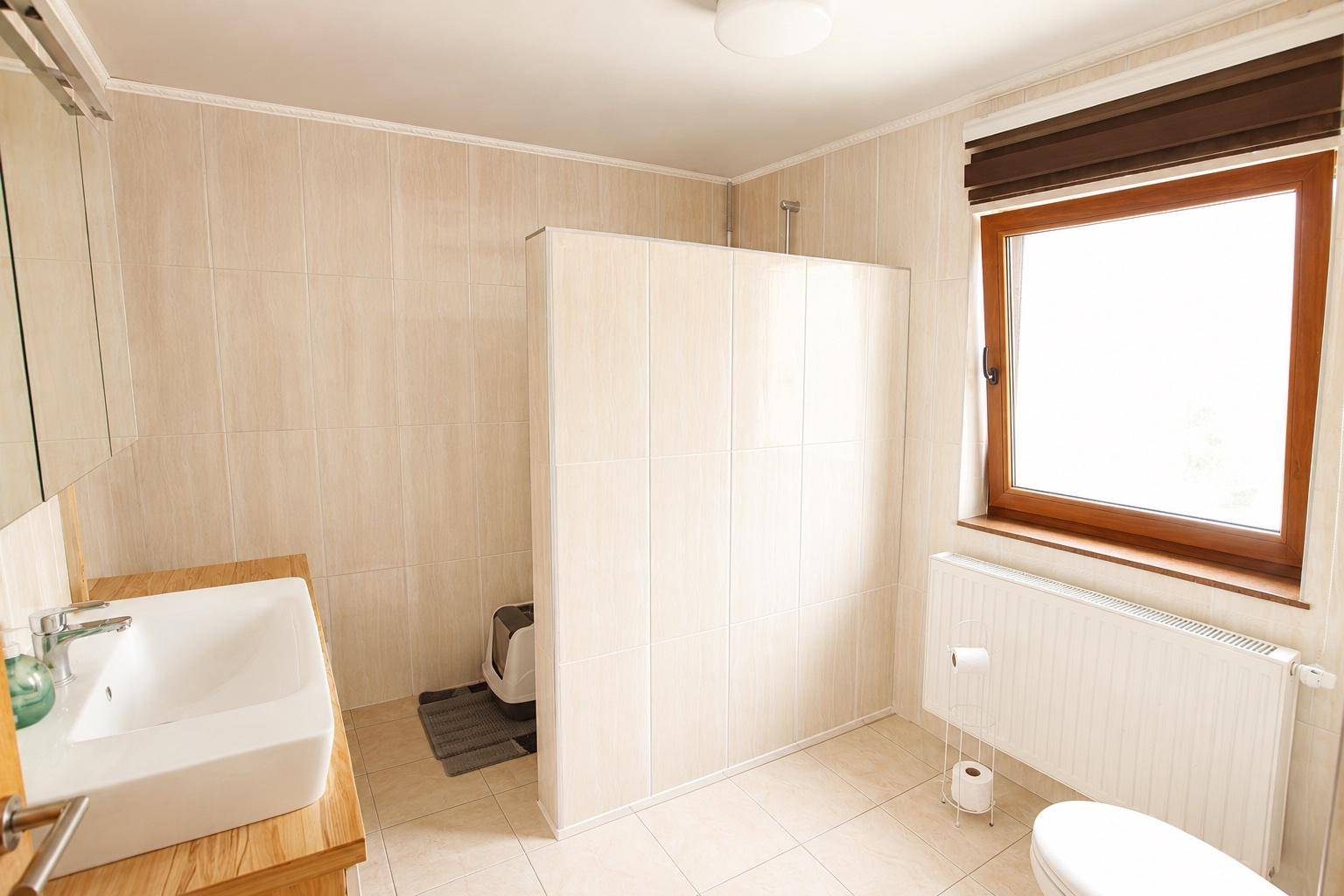 Modernes Badezimmer mit beigefarbenen Fliesen, Waschbecken, Toilette und Duschbereich.