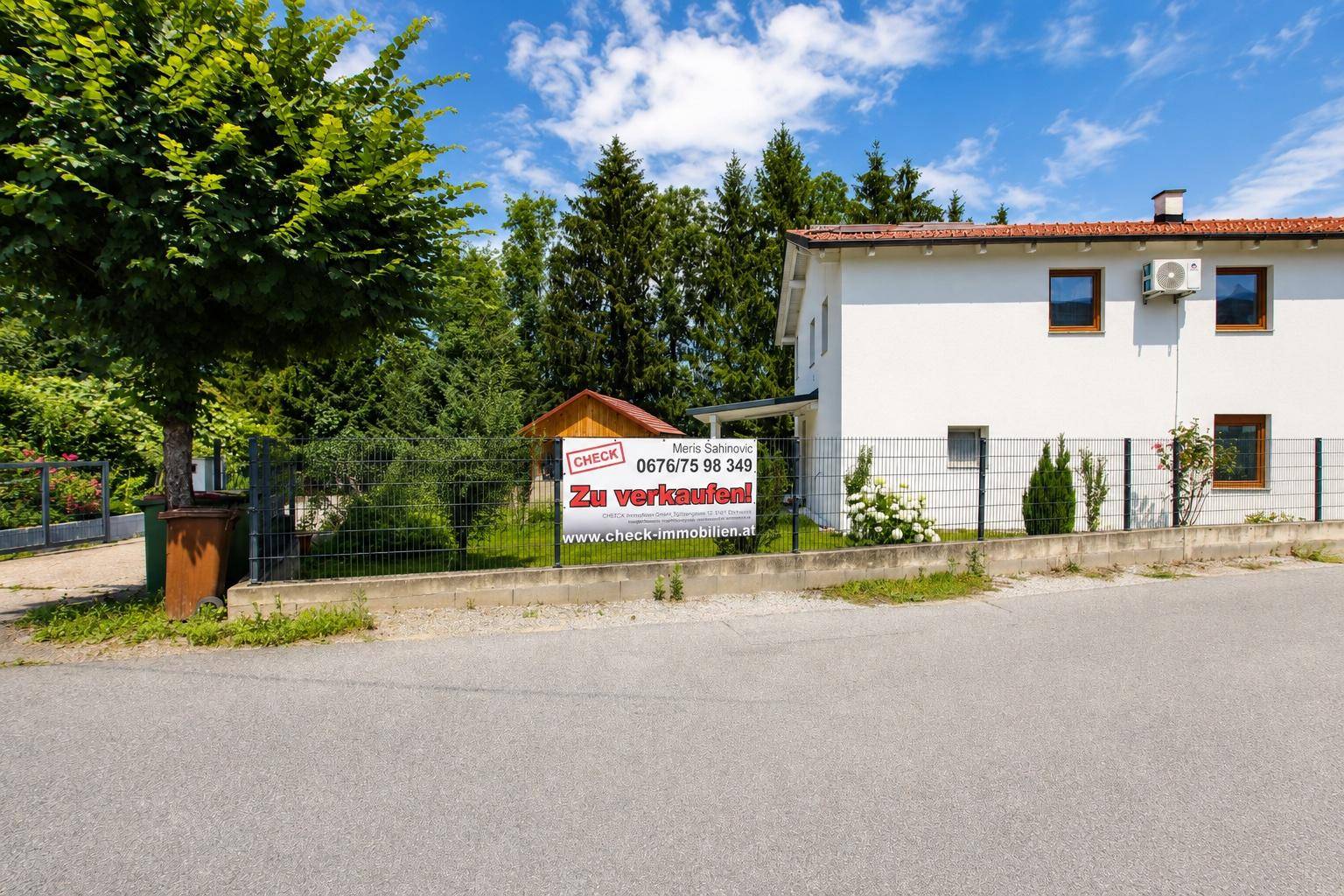 Ansicht des Einfamilienhauses von der Straße mit Verkaufsanzeige und gepflegtem Grundstück.