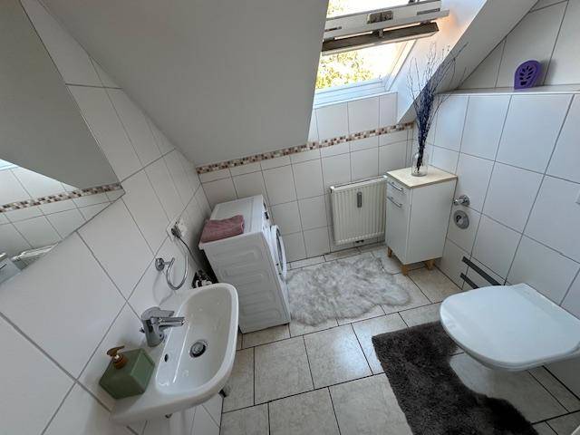 Dachgeschoss-Badezimmer mit Waschbecken, Toilette, Waschmaschine und Dachfenster für natürliches Licht.