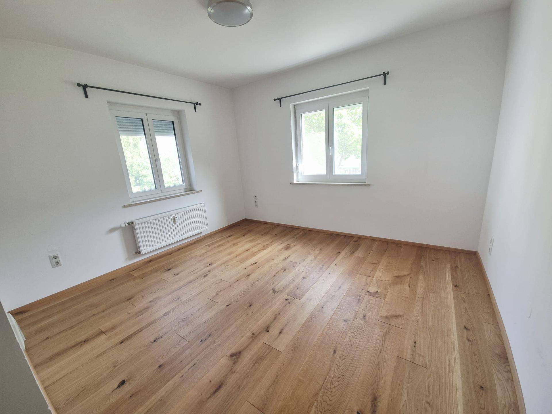 Helles Zimmer mit zwei Fenstern, Holzboden und Rollläden für Privatsphäre.
