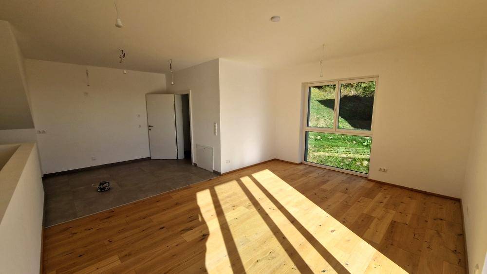 Heller Raum mit Holzboden und einem großen Fenster, das viel Tageslicht hereinlässt.